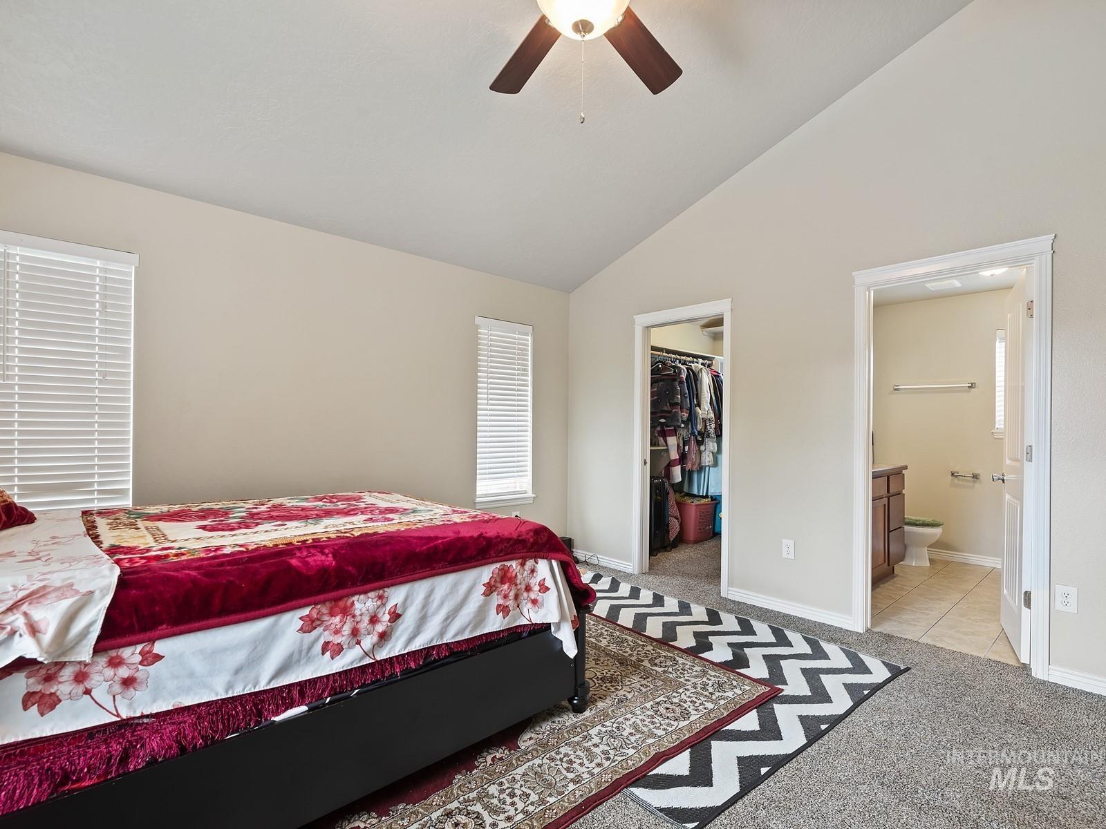 Bedroom with a walk in closet, vaulted ceiling, light carpet, ceiling fan, and ensuite bathroom