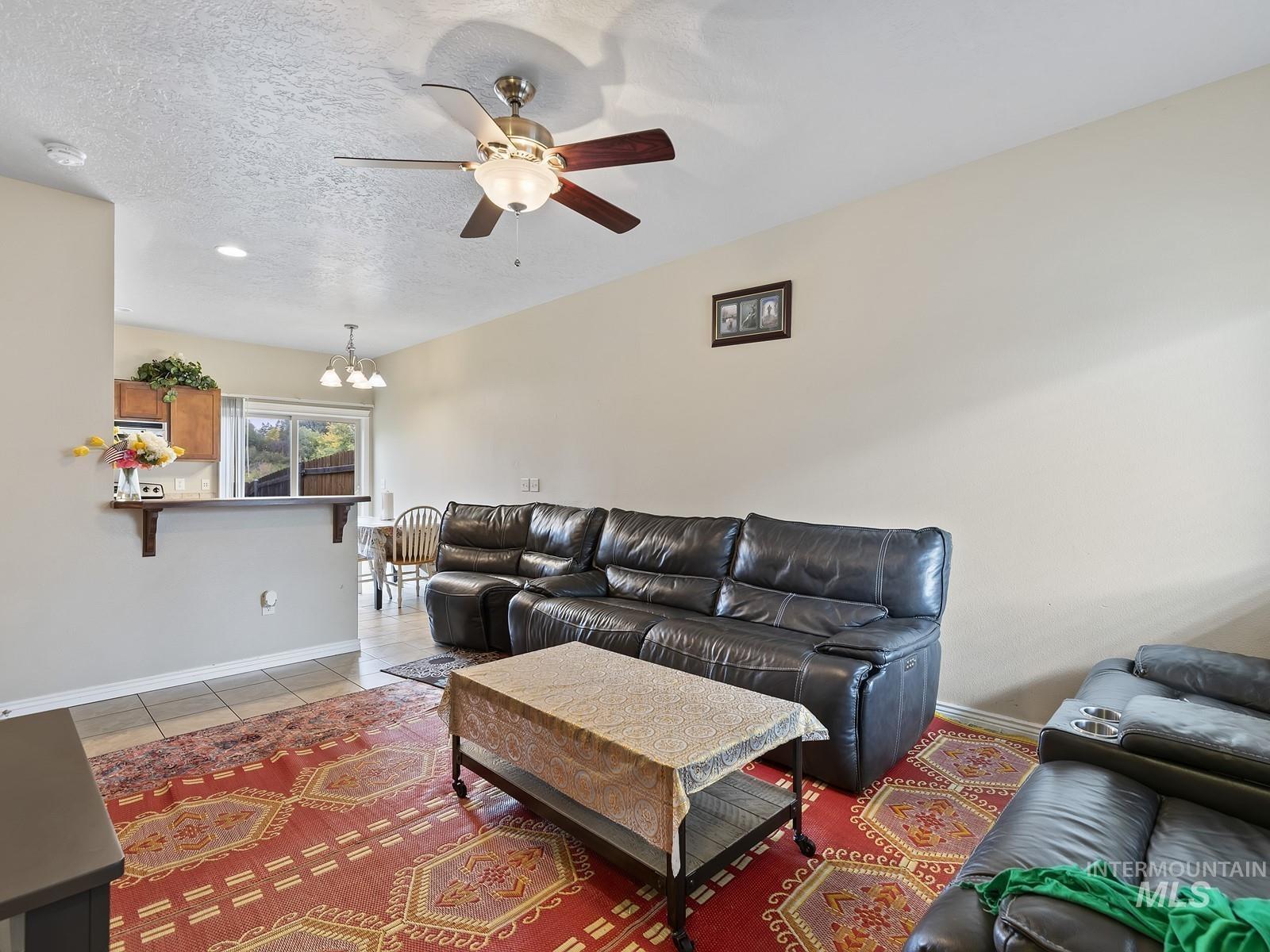 Living room featuring tile patterned floors, a textured ceiling, a ceiling fan, and a chandelier