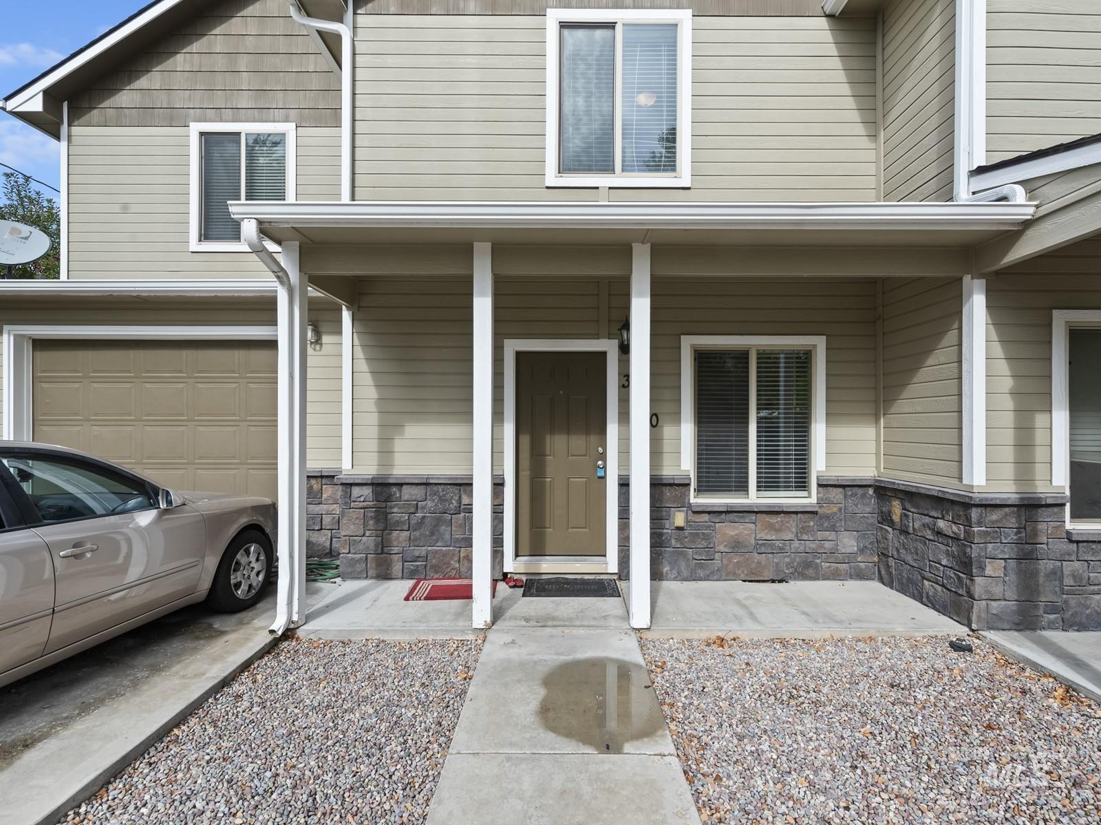 Entrance to property featuring stone siding, covered porch, and an attached garage