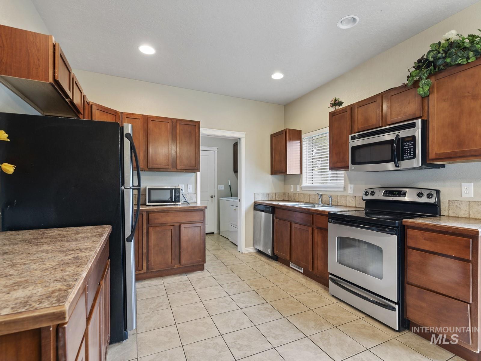Kitchen with stainless steel appliances, brown cabinets, light tile patterned flooring, light countertops, and recessed lighting