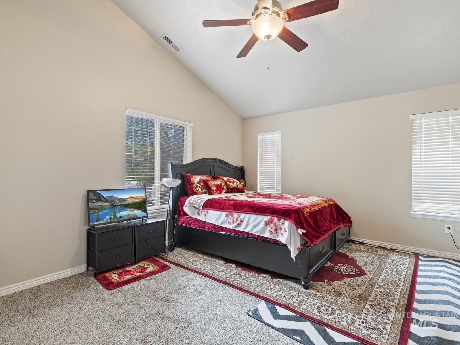Carpeted bedroom featuring ceiling fan and high vaulted ceiling