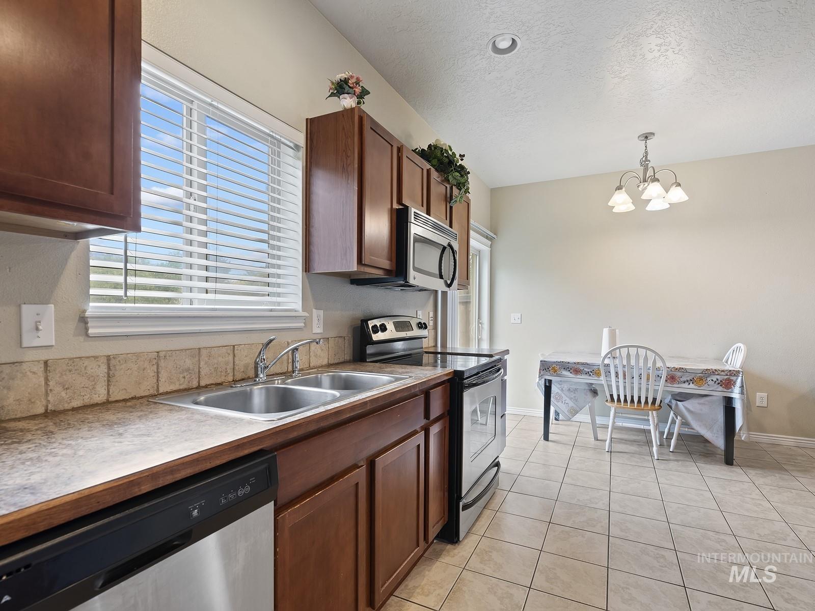 Kitchen with stainless steel appliances, hanging light fixtures, light tile patterned flooring, a chandelier, and a textured ceiling