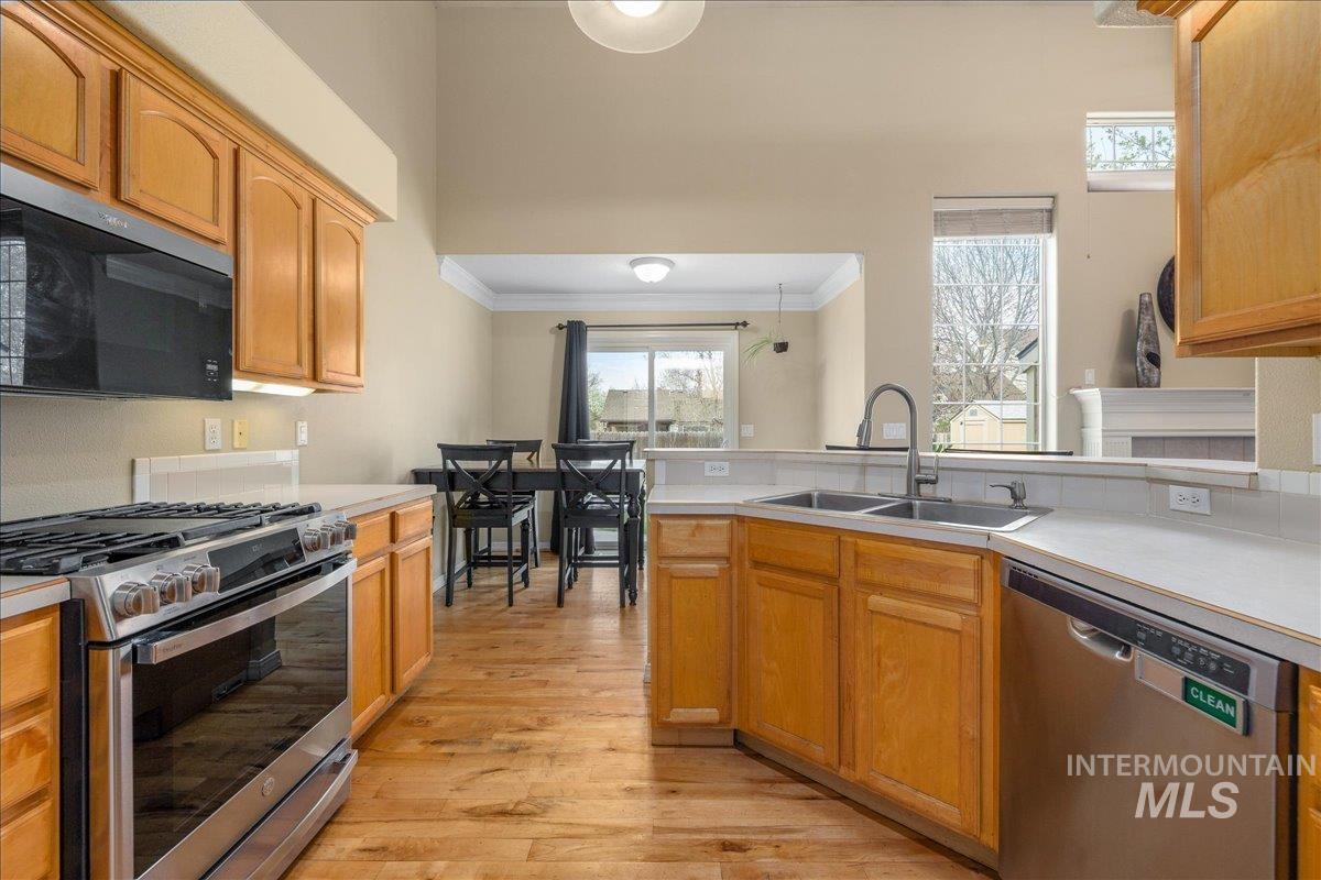 Kitchen with stainless steel appliances, light countertops, light wood finished floors, ornamental molding, and a peninsula