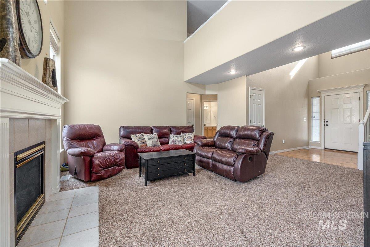 Living area featuring light colored carpet, a tiled fireplace, and a high ceiling