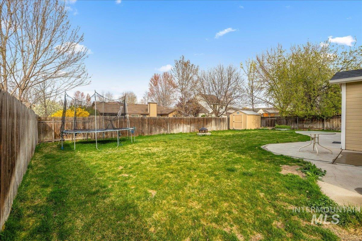 Fenced backyard featuring a shed, a patio, and a trampoline