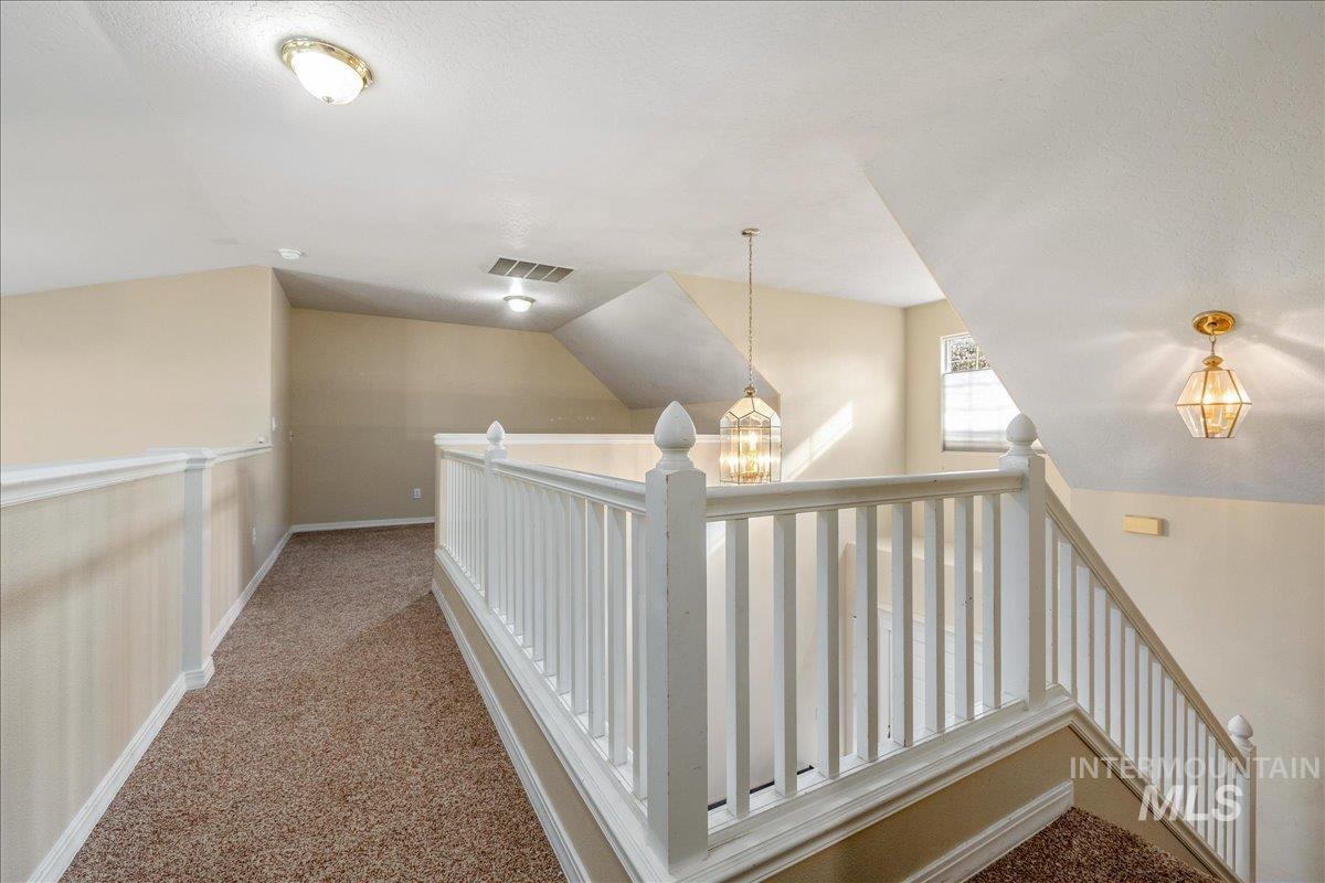 Hallway featuring light colored carpet and a chandelier