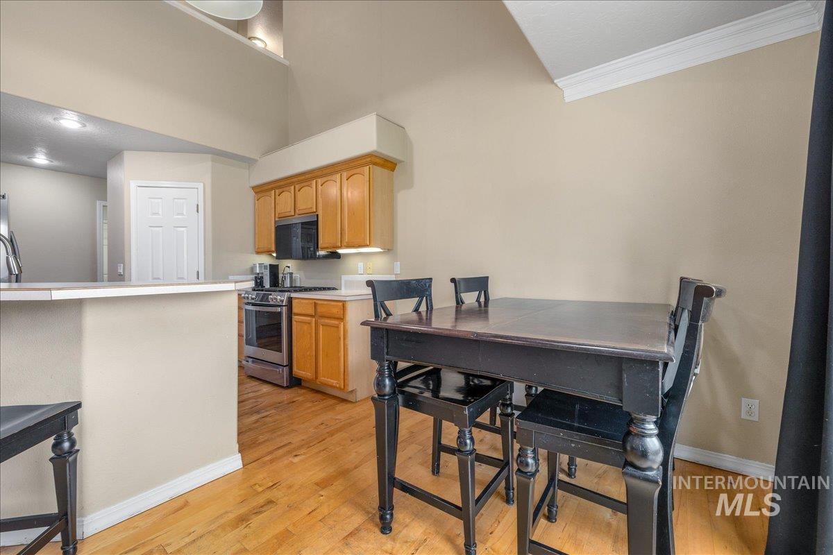 Kitchen featuring light countertops, stainless steel range with gas stovetop, black microwave, light wood-style flooring, and ornamental molding