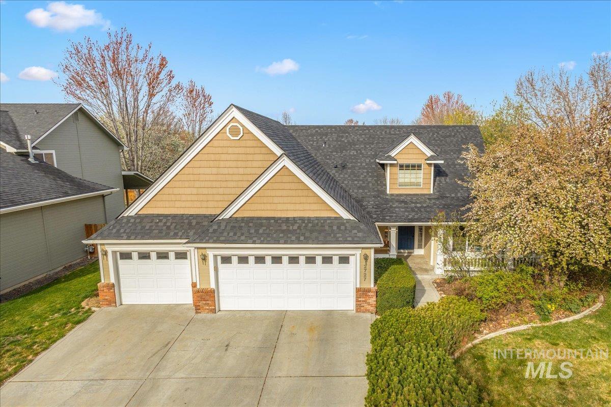 Traditional-style home featuring roof with shingles, brick siding, driveway, and a garage