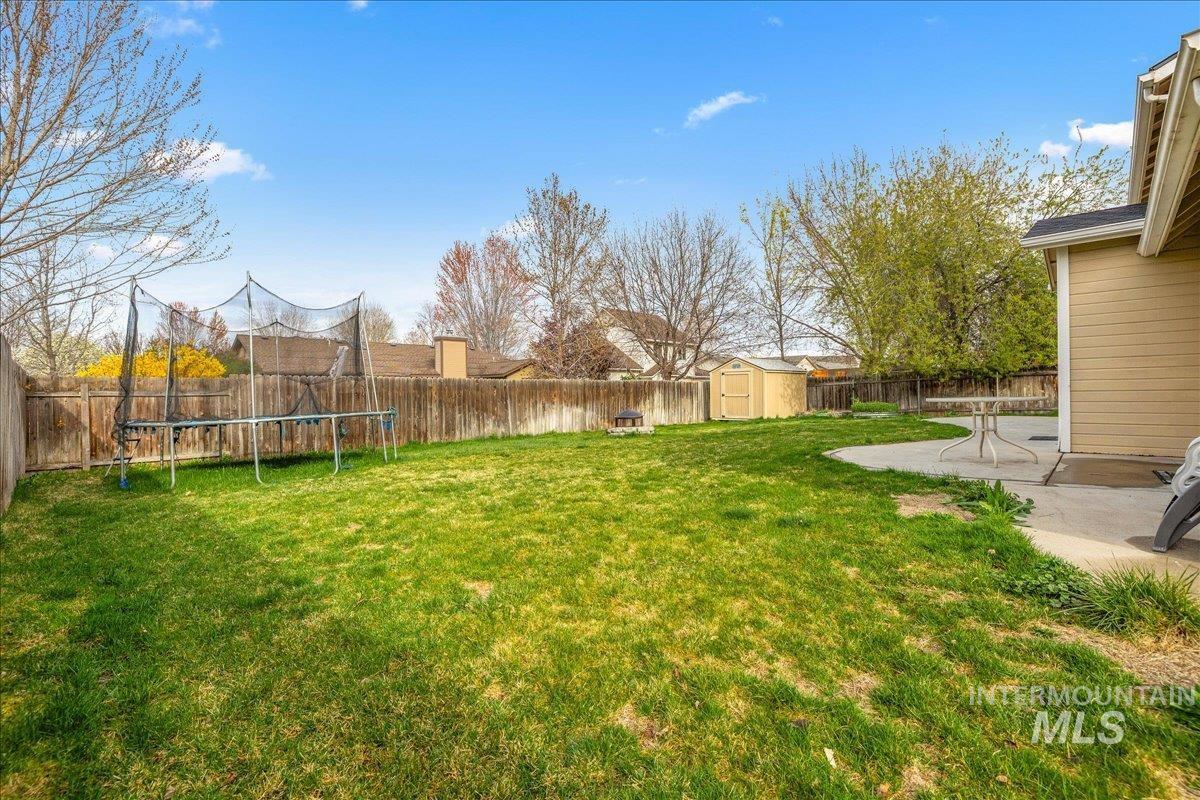 Fenced backyard featuring a trampoline, a shed, and a patio