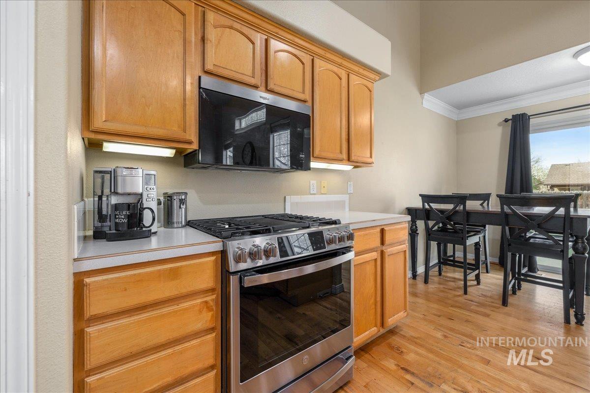 Kitchen with stainless steel range with gas stovetop, light countertops, crown molding, and light wood finished floors