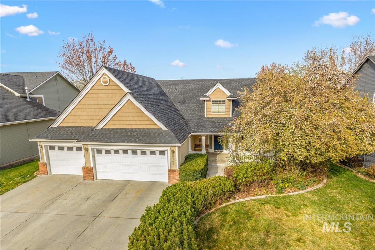 View of front of house featuring an attached garage, a shingled roof, driveway, a front yard, and brick siding