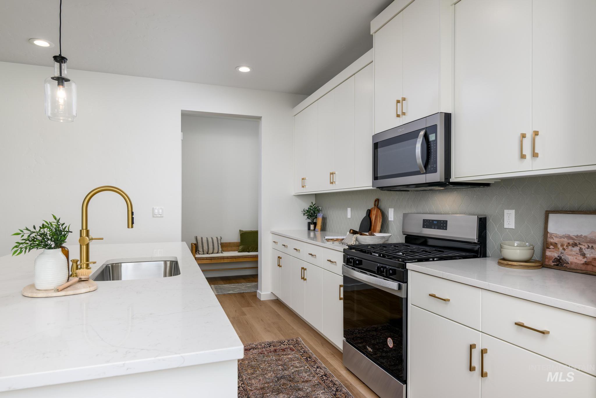 Kitchen with appliances with stainless steel finishes, white cabinetry, light wood-style floors, hanging light fixtures, and backsplash