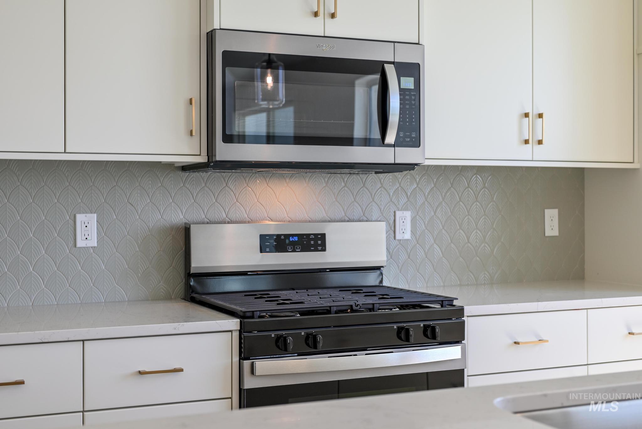 Kitchen featuring stainless steel appliances, decorative backsplash, white cabinetry, and light stone countertops