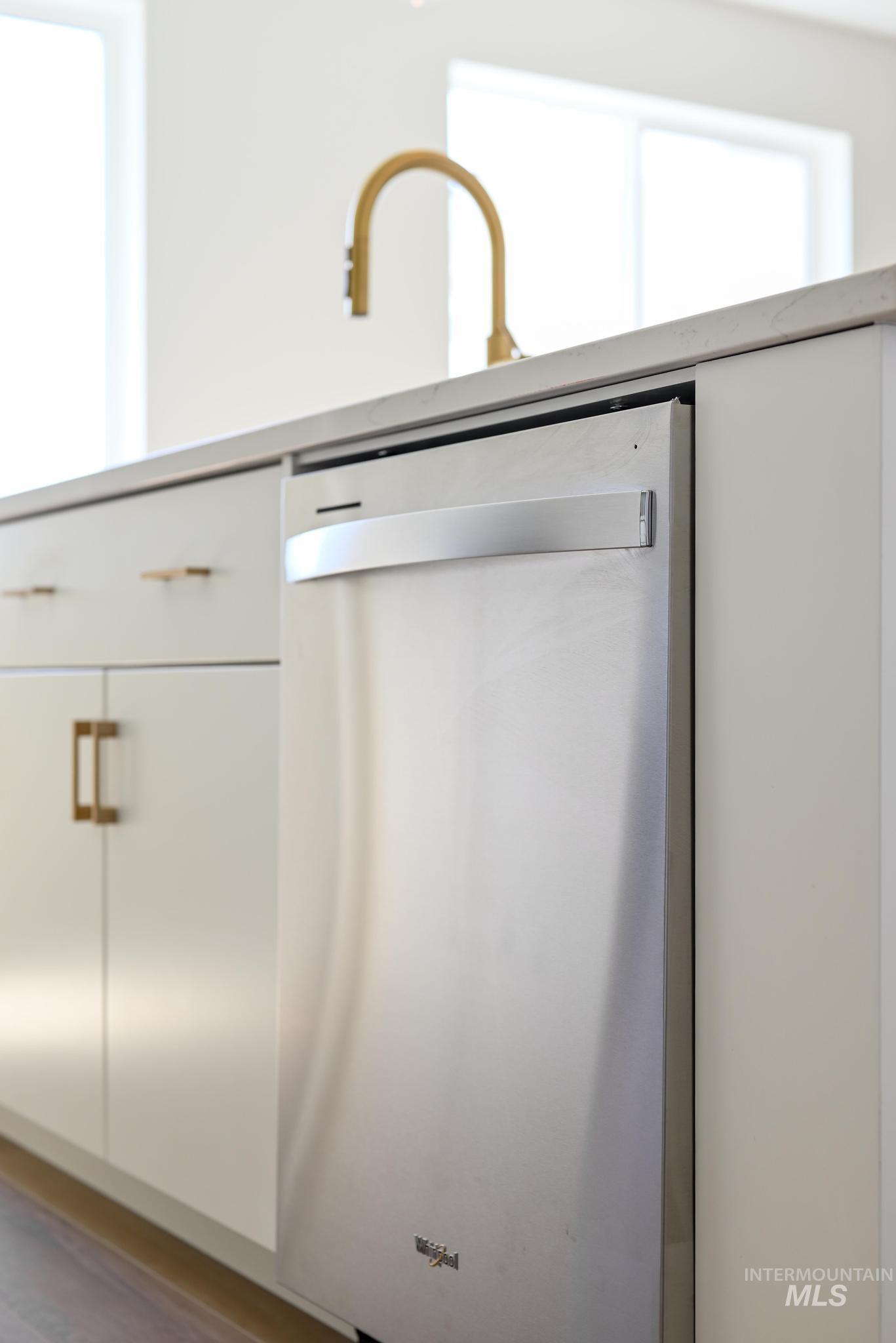 Kitchen view of dishwasher, white cabinetry, light countertops, and wood finished floors