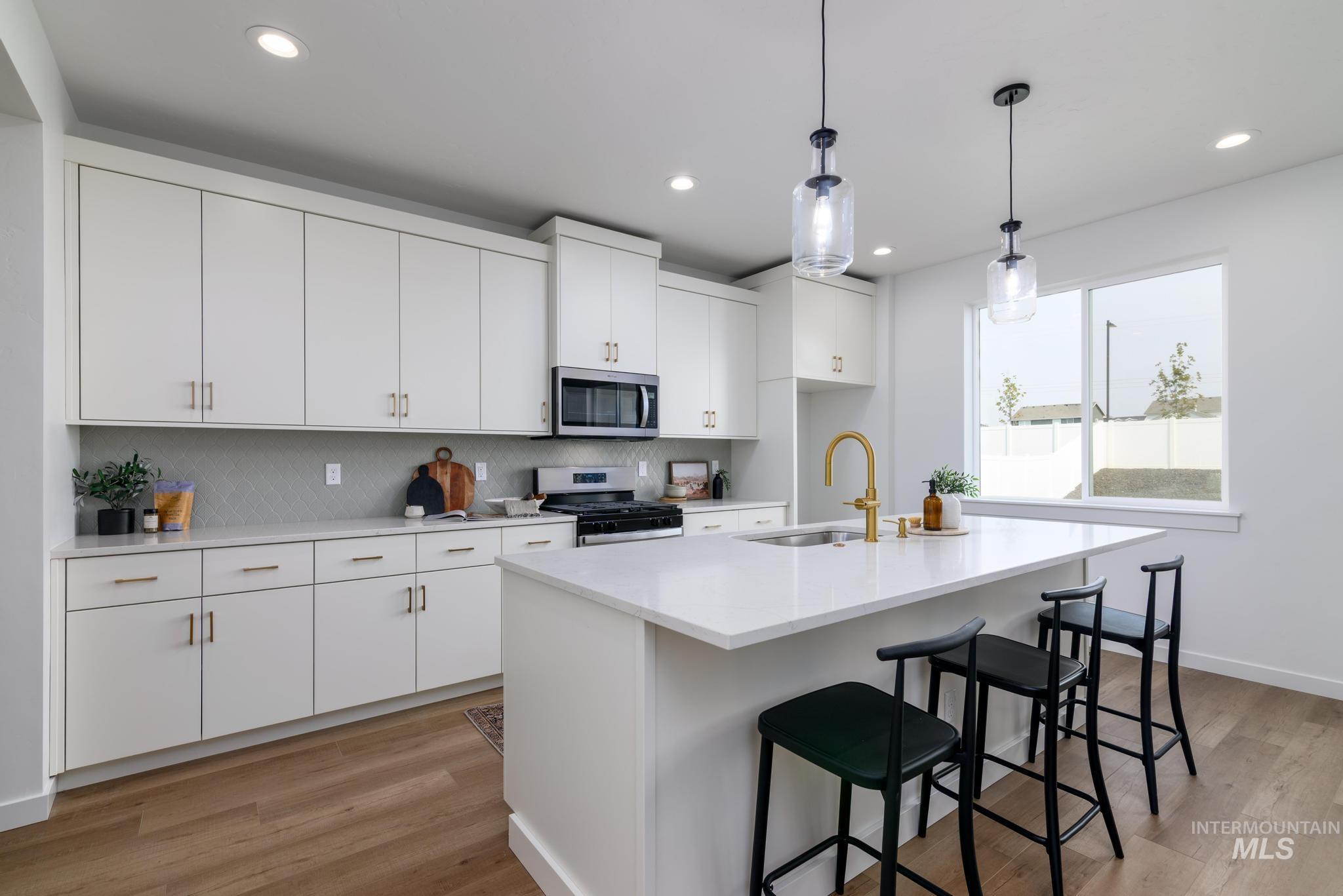 Kitchen featuring pendant lighting, light wood-style flooring, white cabinets, a breakfast bar, and stainless steel appliances