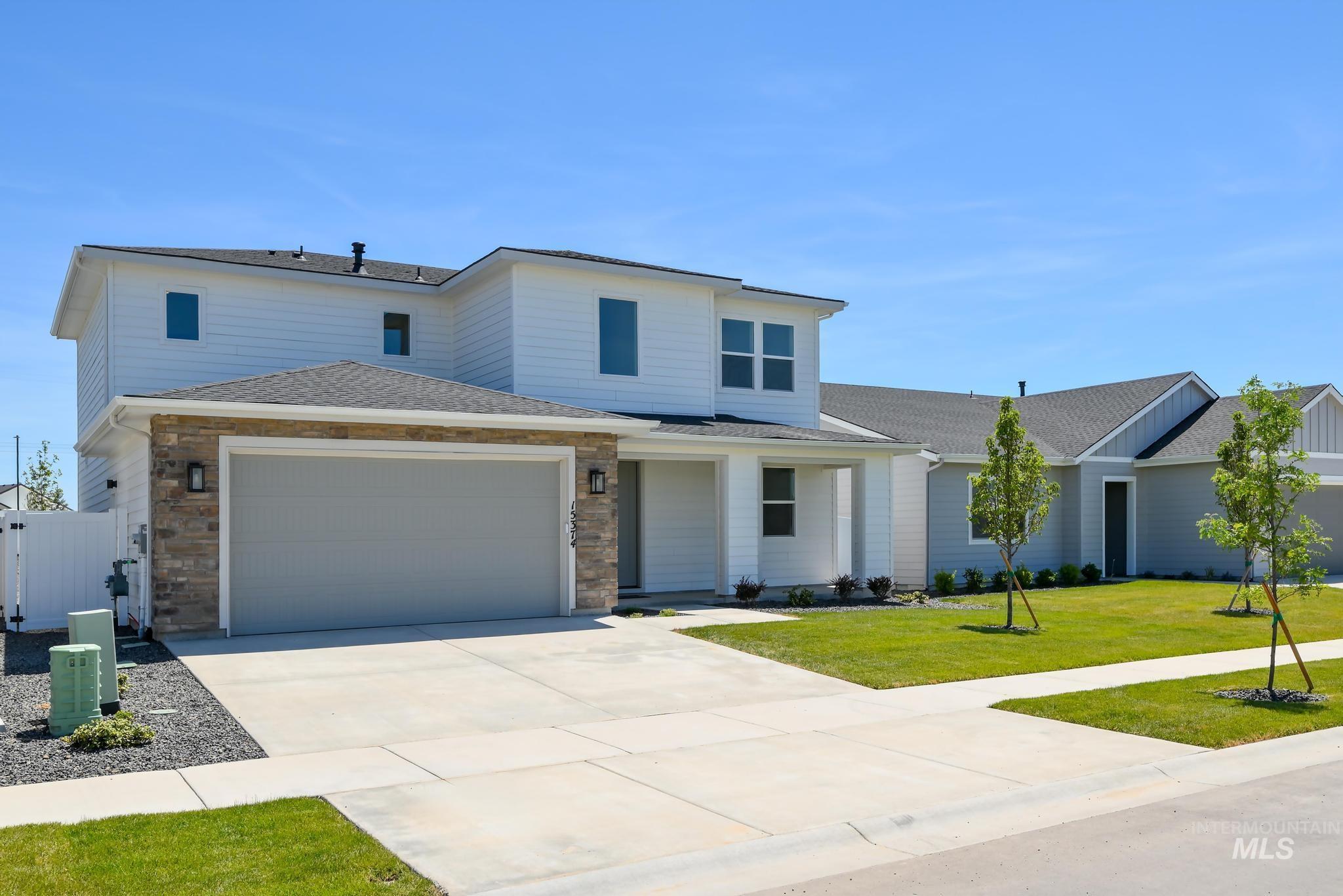 View of front facade featuring driveway, a shingled roof, a garage, stone siding, and a front lawn