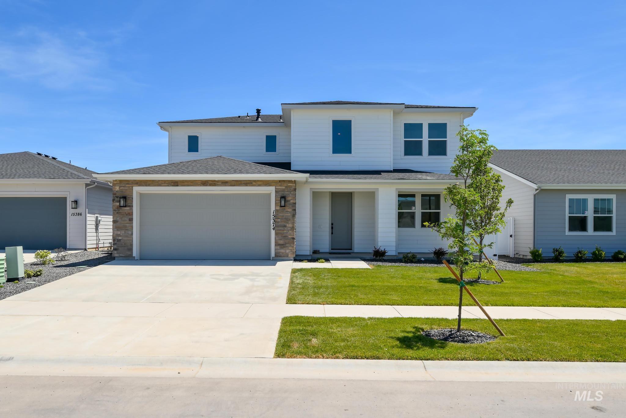View of front of home featuring roof with shingles, driveway, an attached garage, a front lawn, and stone siding