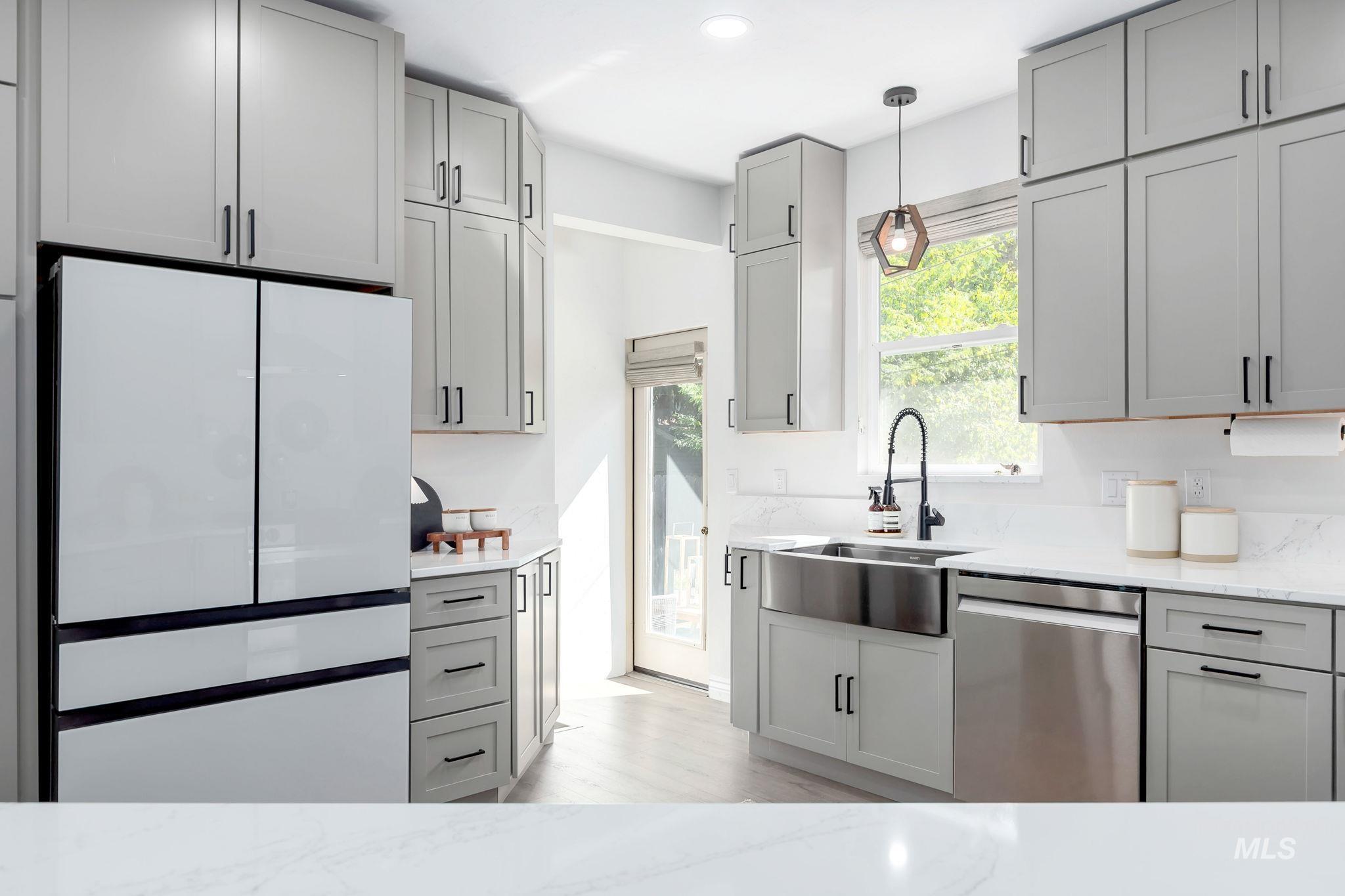 Kitchen featuring gray cabinets, stainless steel dishwasher, freestanding refrigerator, light stone countertops, and pendant lighting