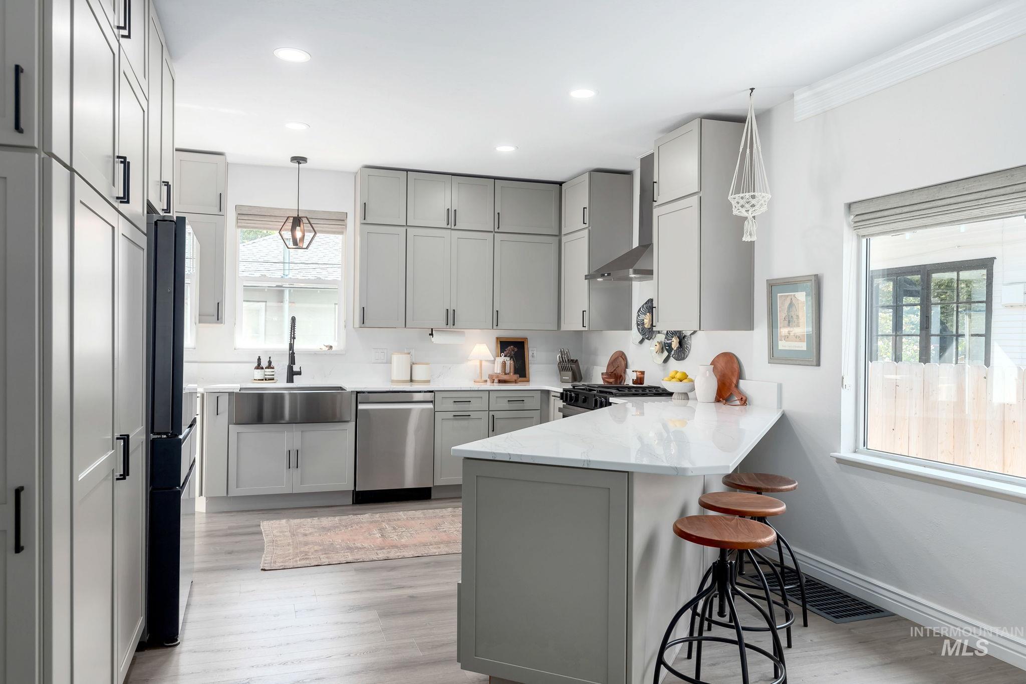 Kitchen with gray cabinets, a peninsula, light stone countertops, a kitchen breakfast bar, and black appliances