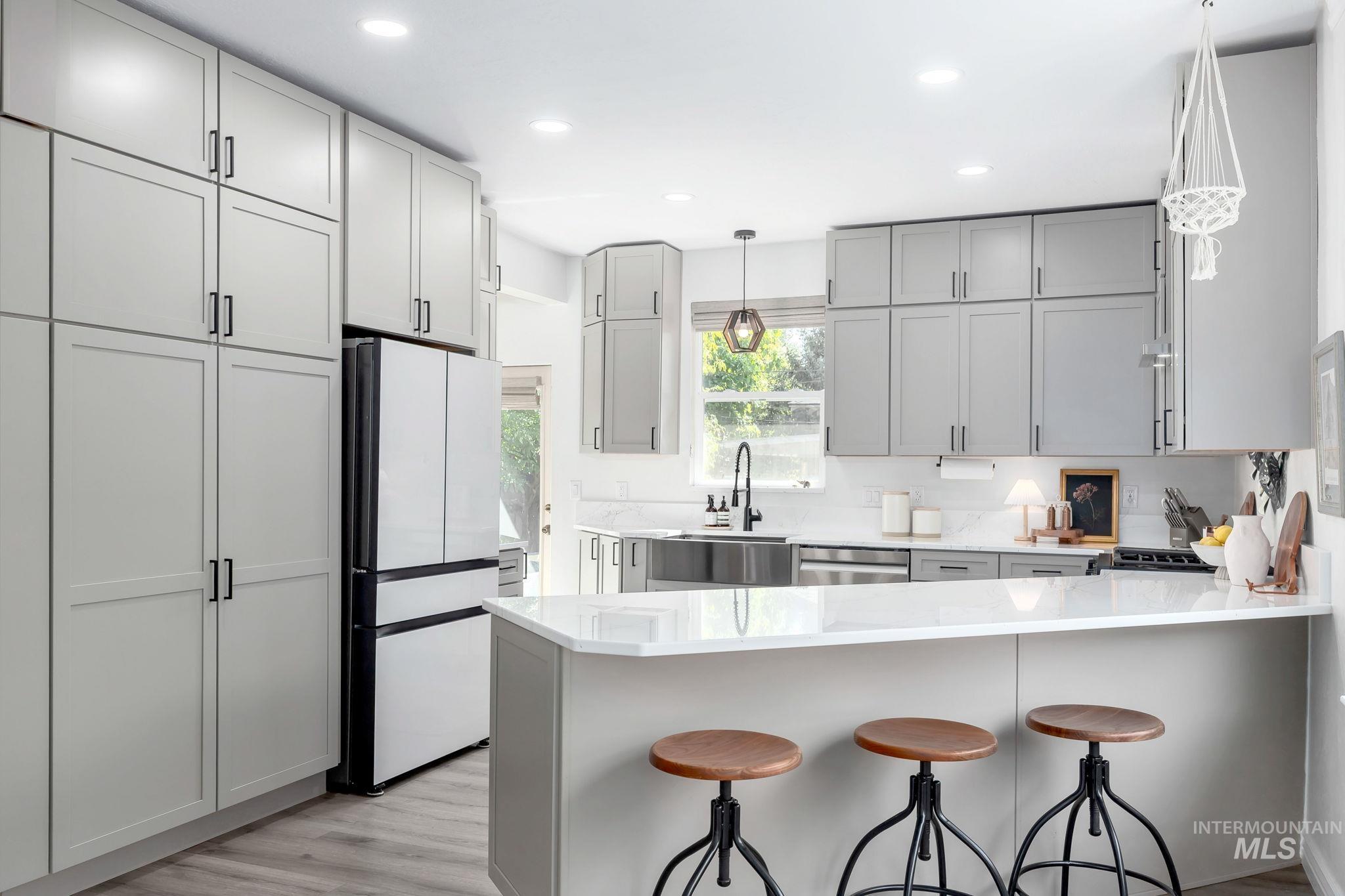 Kitchen featuring gray cabinets, a peninsula, a kitchen bar, hanging light fixtures, and light stone countertops