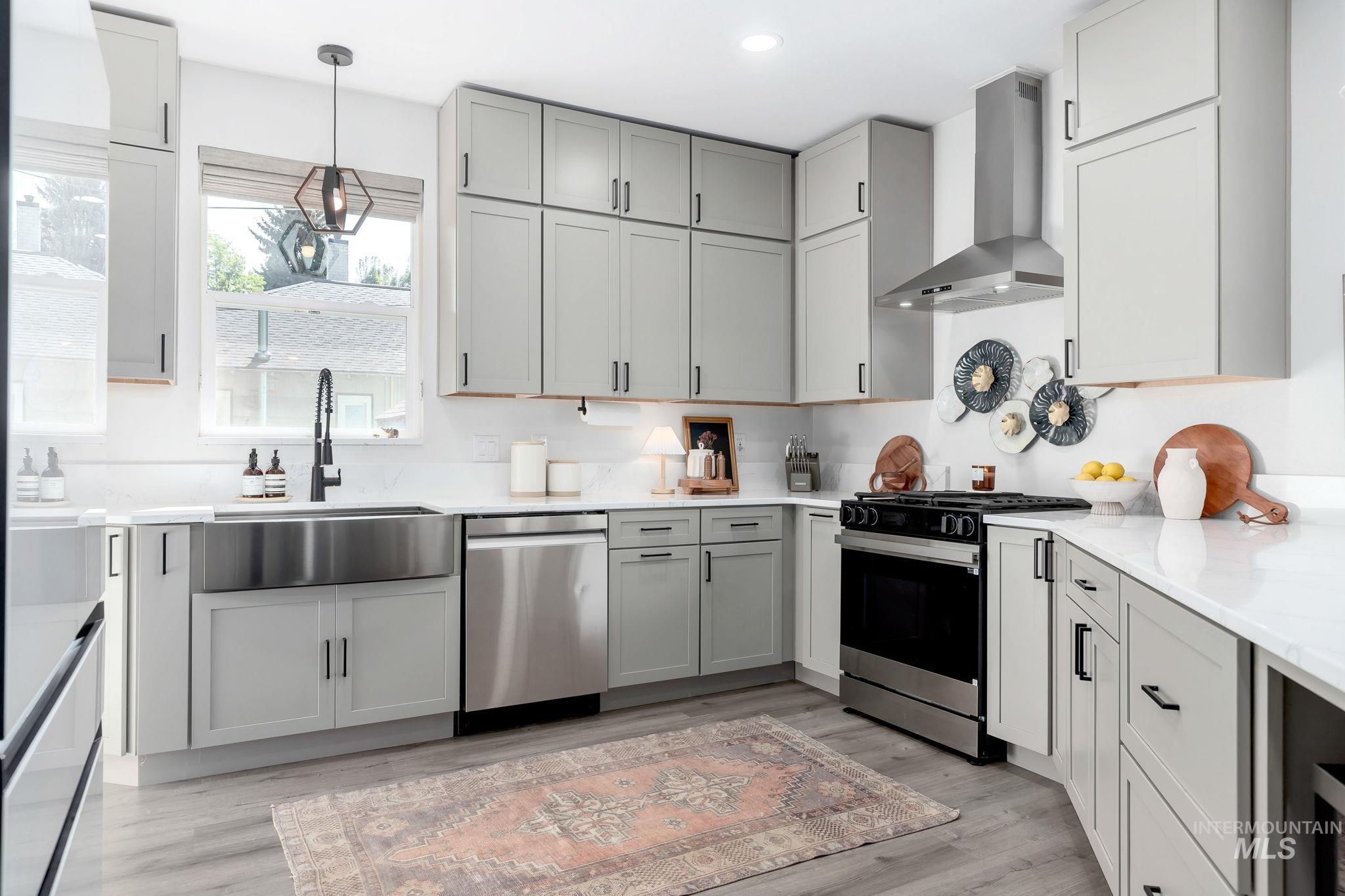 Kitchen with wall chimney range hood, stainless steel appliances, pendant lighting, gray cabinets, and light stone countertops