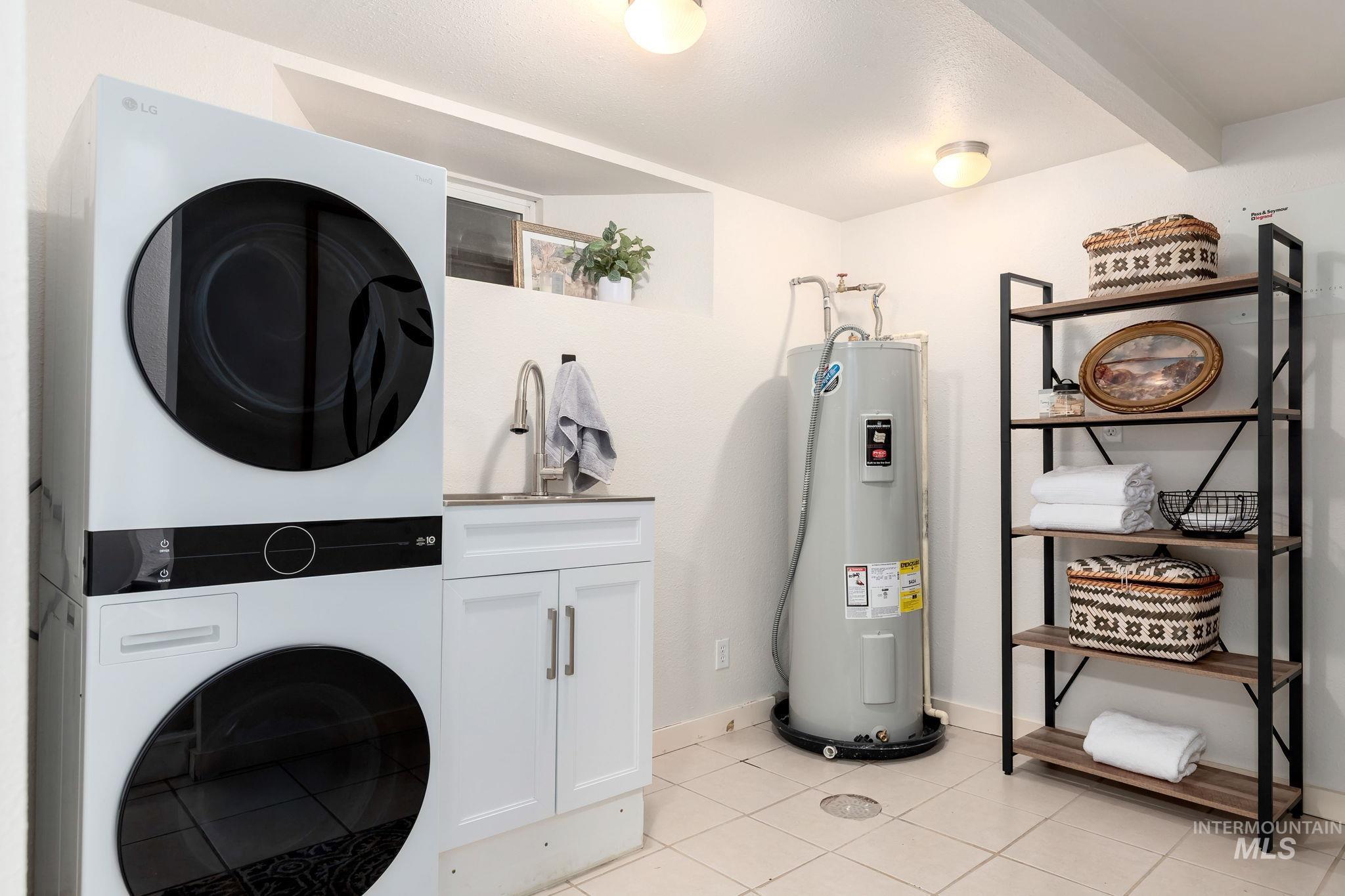 Laundry room with cabinet space, light tile patterned flooring, water heater, and stacked washing machine and dryer