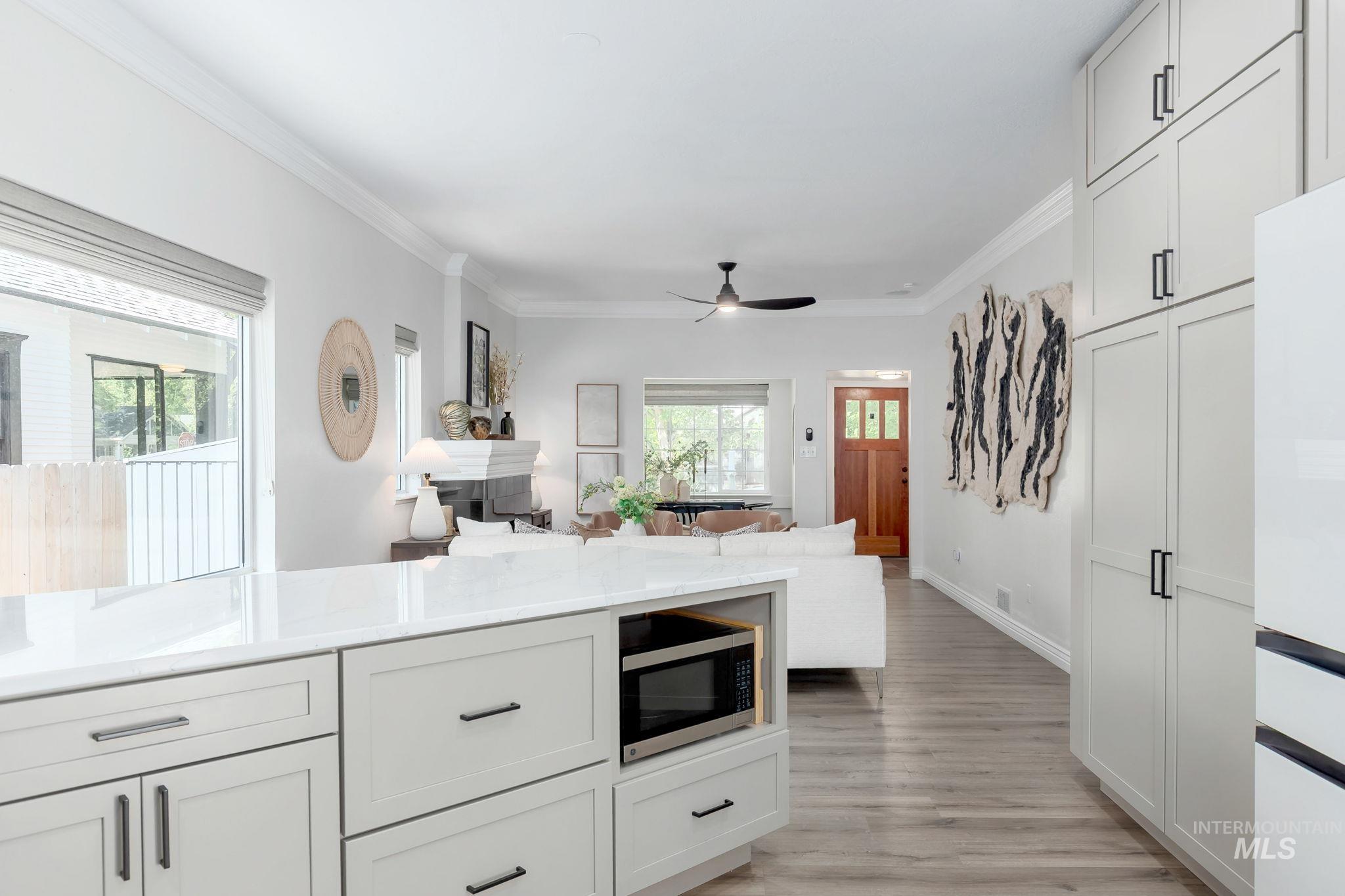 Kitchen featuring open floor plan, ornamental molding, light stone counters, light wood-type flooring, and freestanding refrigerator