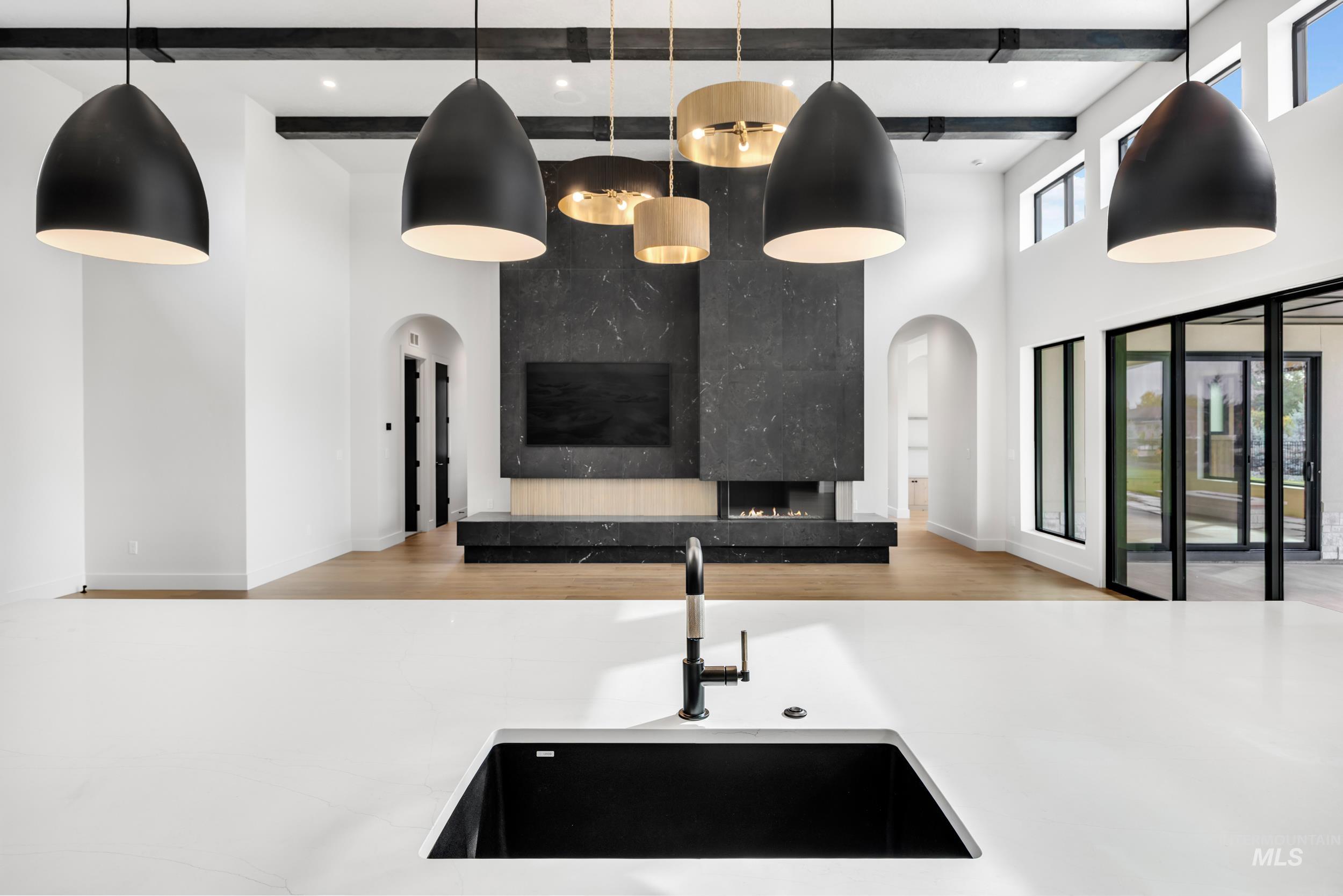 Kitchen featuring open floor plan, decorative light fixtures, light wood-type flooring, light stone counters, and beamed ceiling