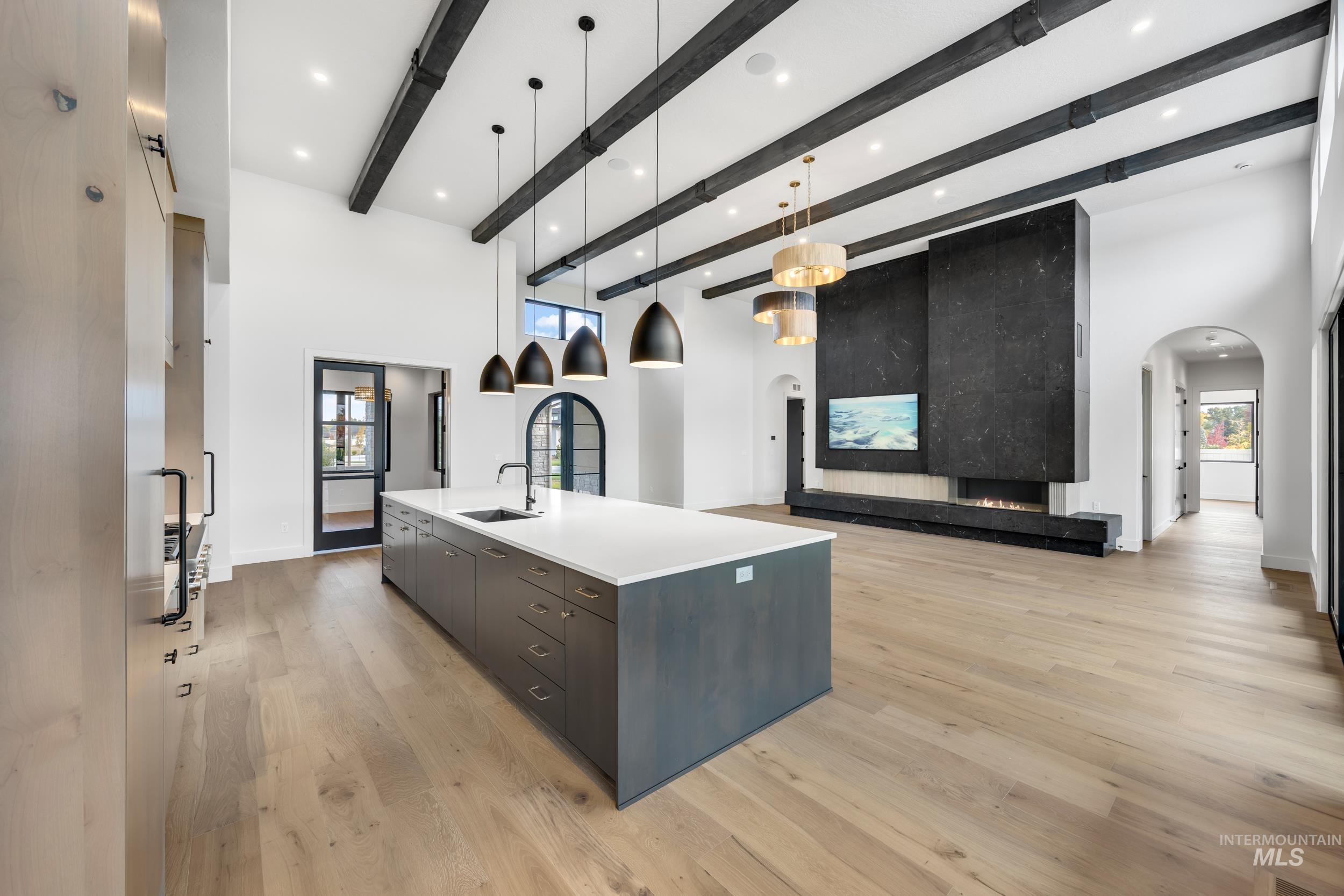 Kitchen featuring arched walkways, hanging light fixtures, a large island with sink, light wood-style floors, and open floor plan