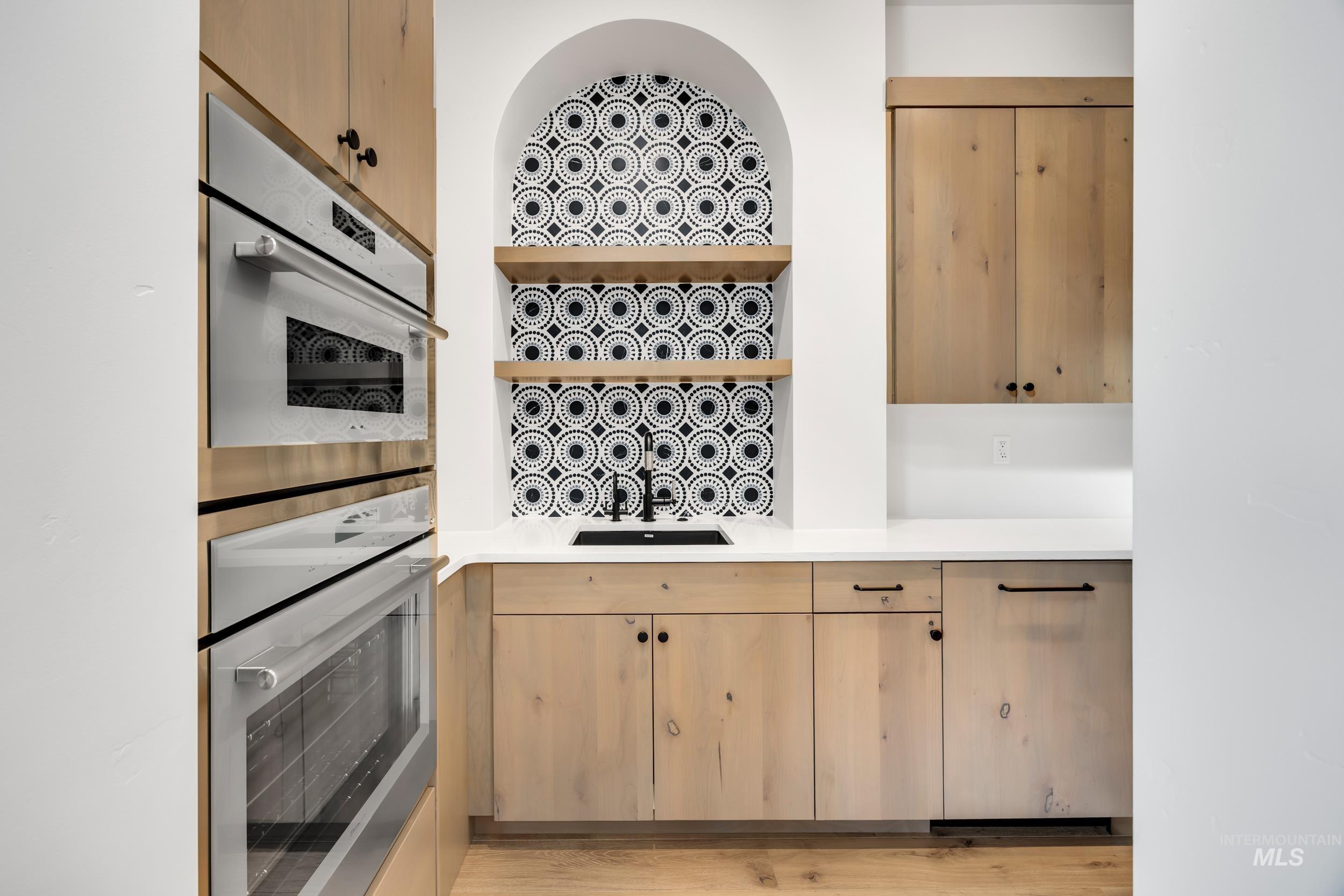 Kitchen with open shelves, double oven, light brown cabinets, light stone countertops, and light wood finished floors