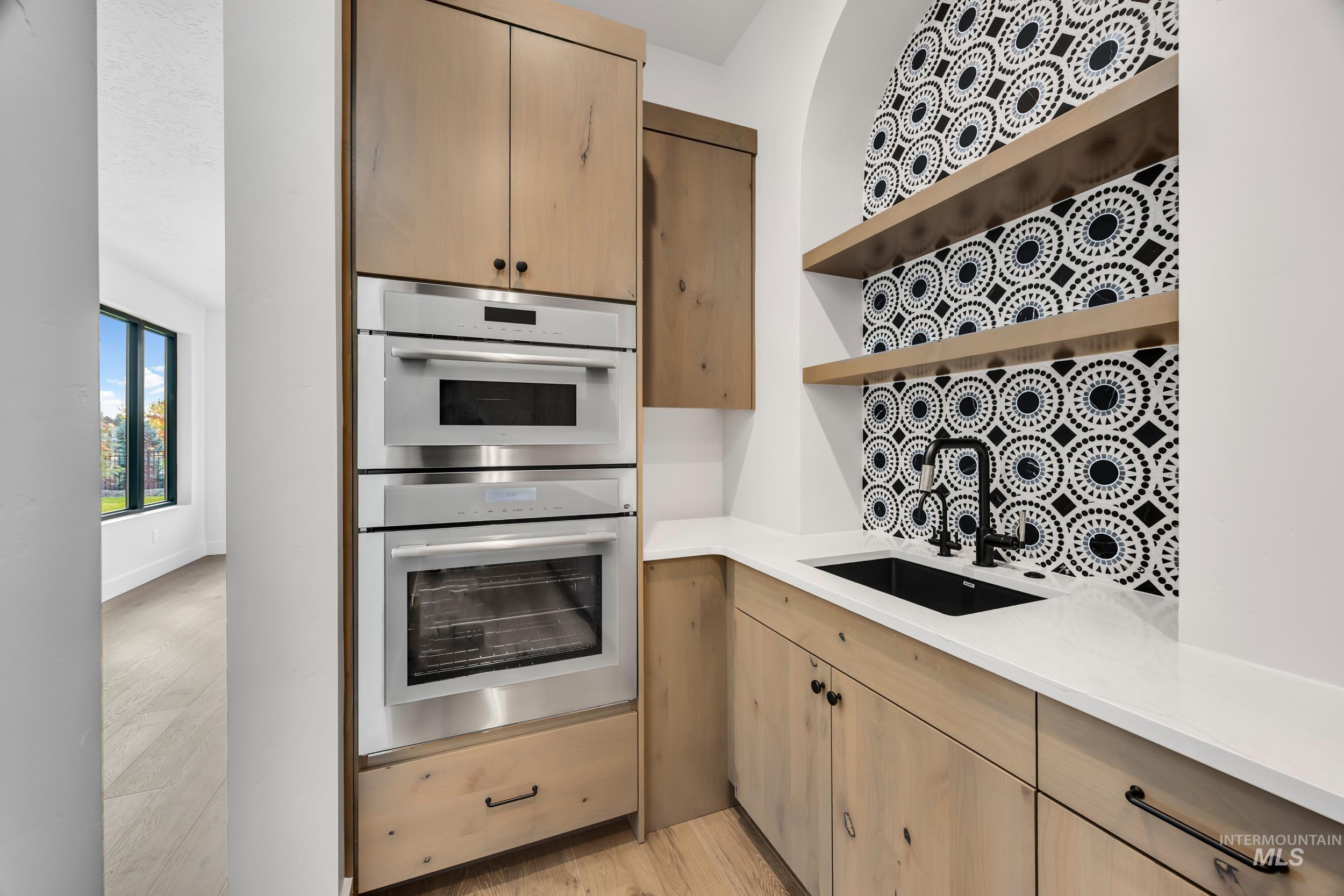 Kitchen with open shelves, stainless steel double oven, light brown cabinetry, and light wood-type flooring