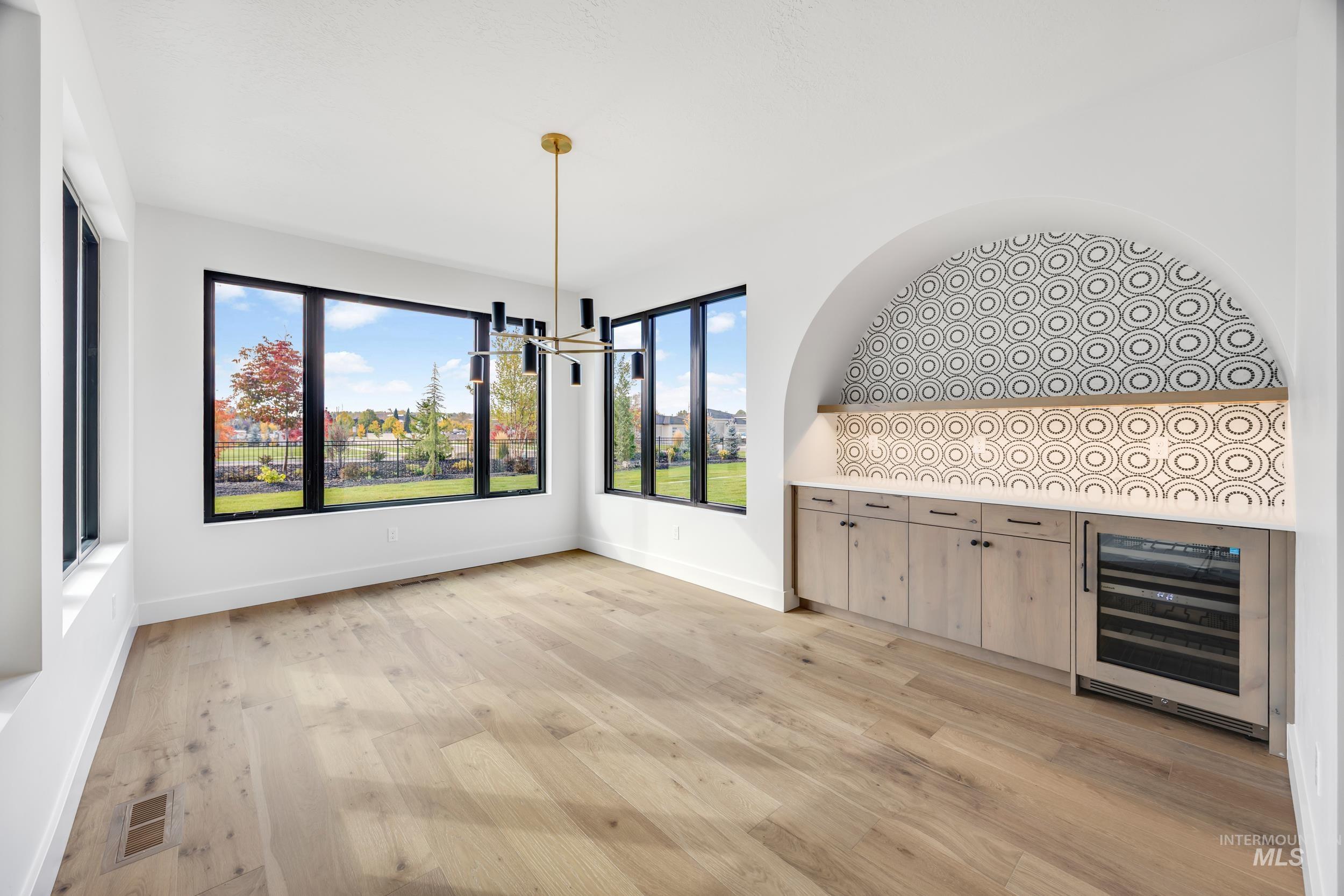 Unfurnished dining area featuring beverage cooler, light wood-style flooring, and a chandelier