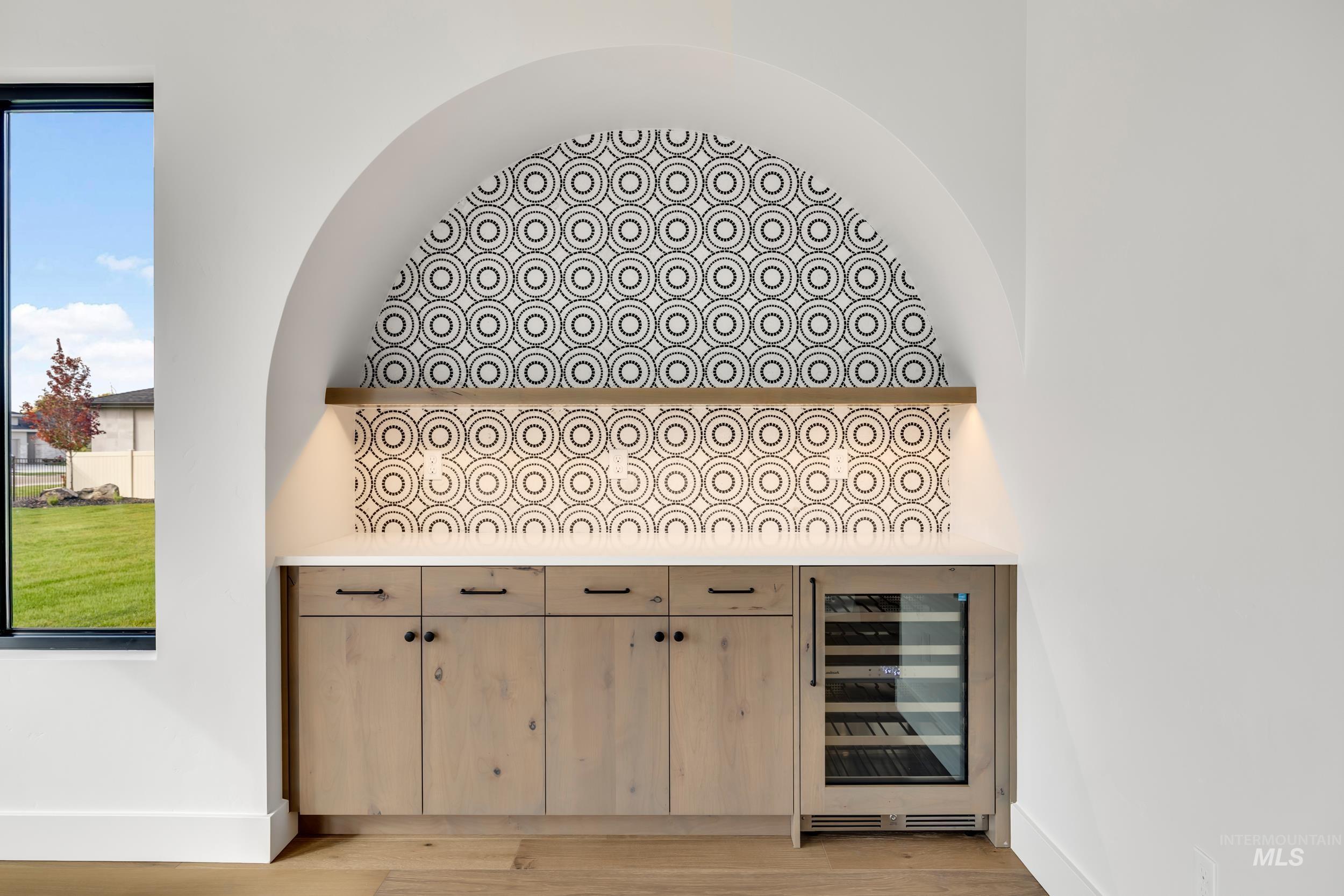 Bar with light brown cabinetry, wine cooler, light wood-style floors, and light stone countertops