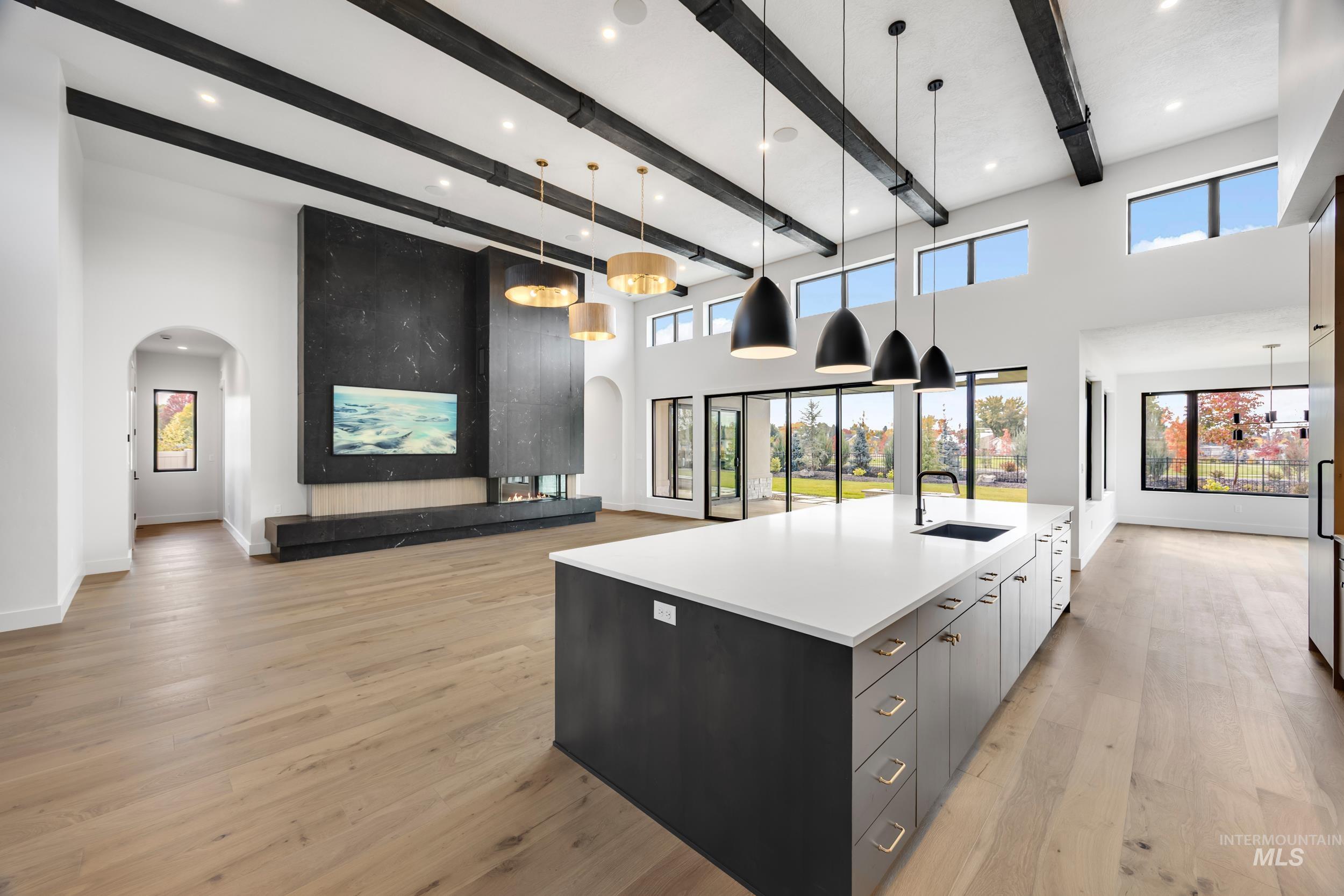 Kitchen featuring arched walkways, decorative light fixtures, open floor plan, modern cabinets, and a large island with sink
