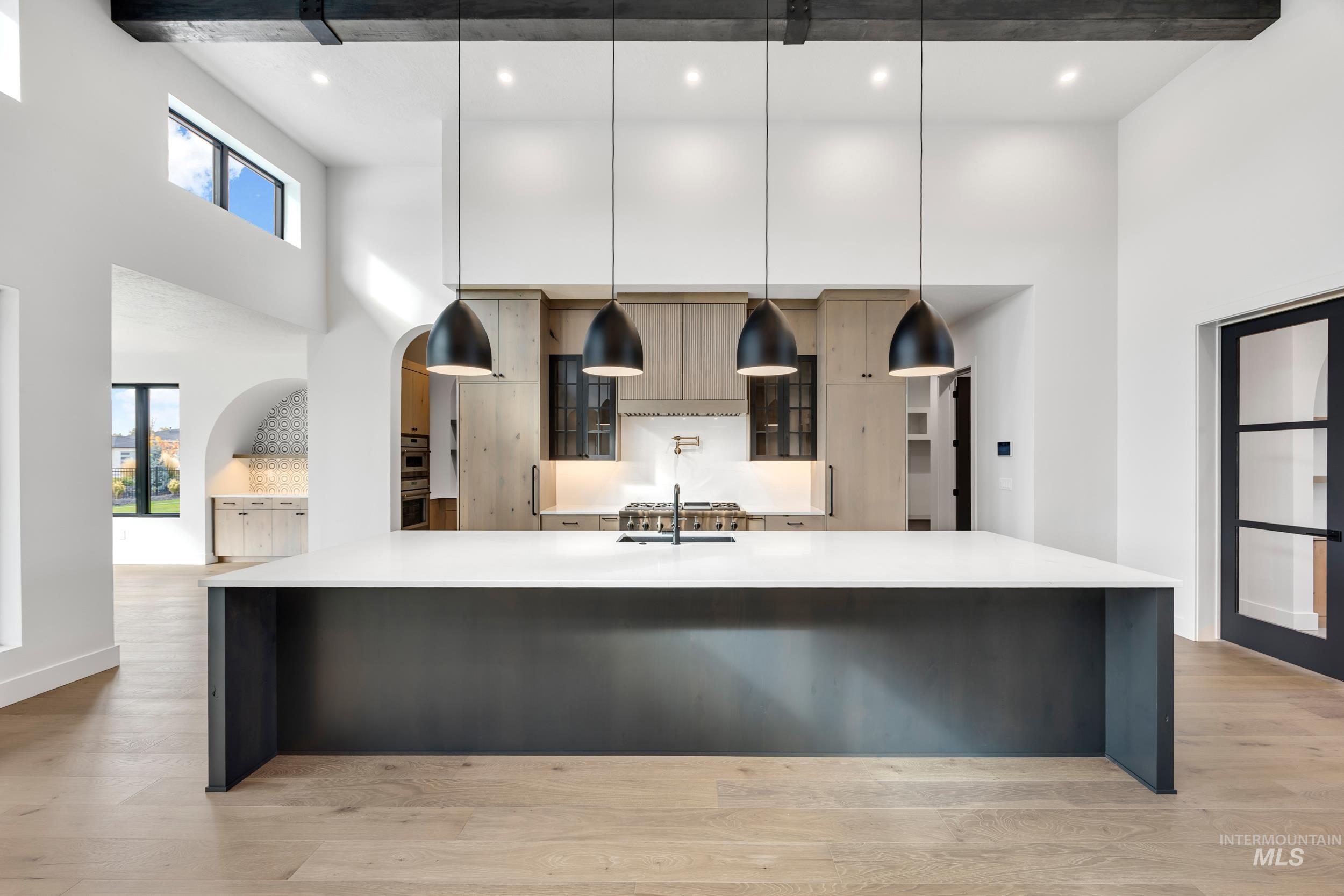 Kitchen with a high ceiling, decorative light fixtures, light wood-style flooring, light stone countertops, and a breakfast bar
