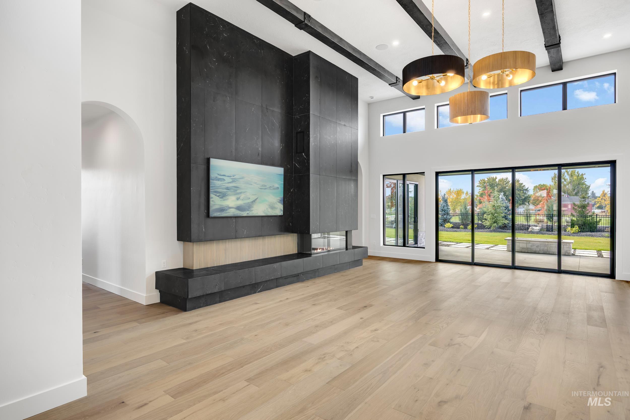 Unfurnished living room with beam ceiling, light wood-type flooring, healthy amount of natural light, a high ceiling, and arched walkways