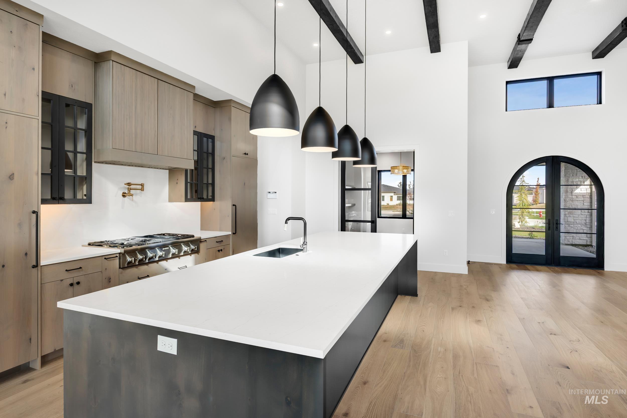 Kitchen featuring glass insert cabinets, hanging light fixtures, light wood-type flooring, a large island with sink, and beam ceiling