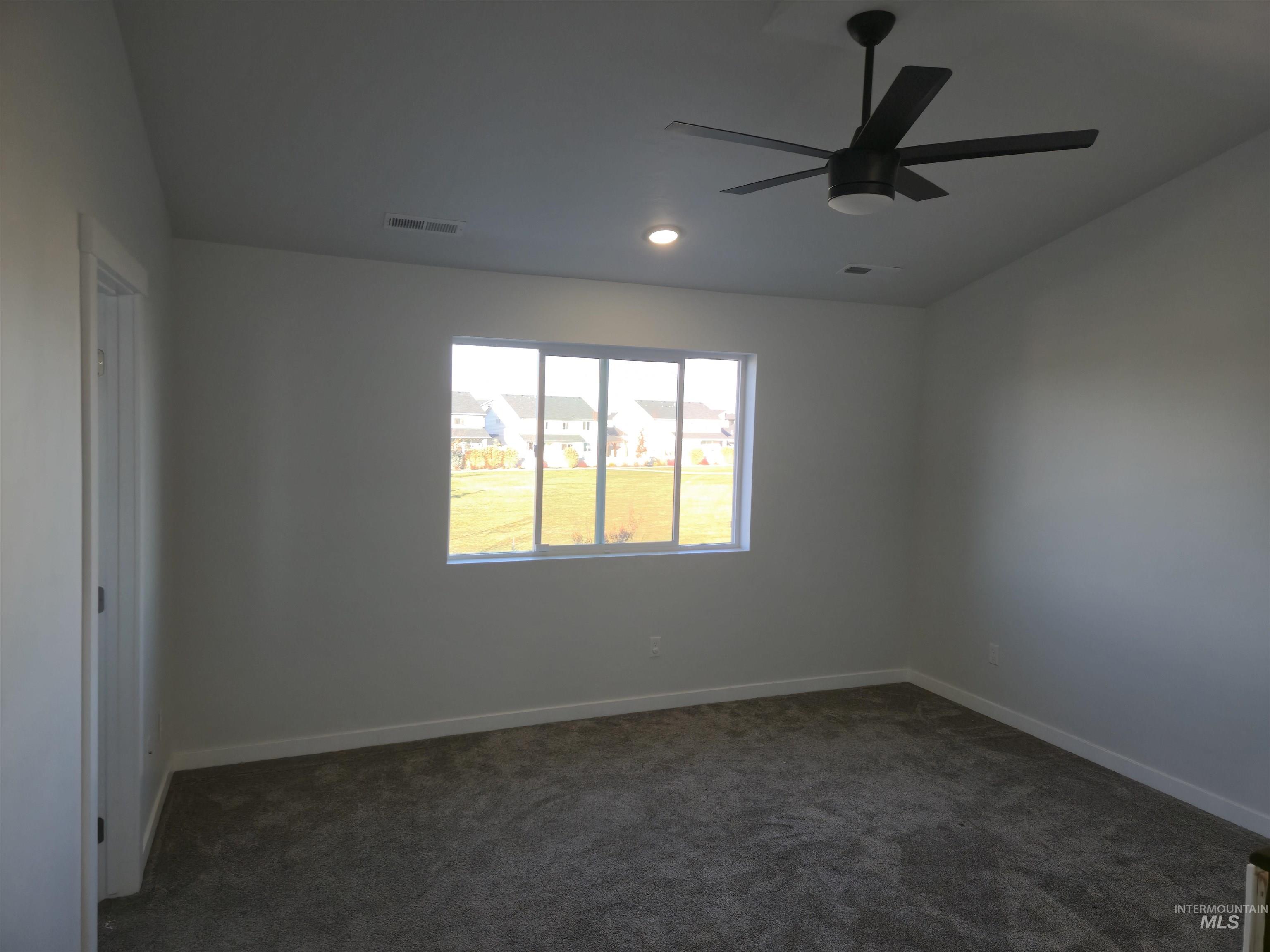Unfurnished room featuring dark carpet and a ceiling fan