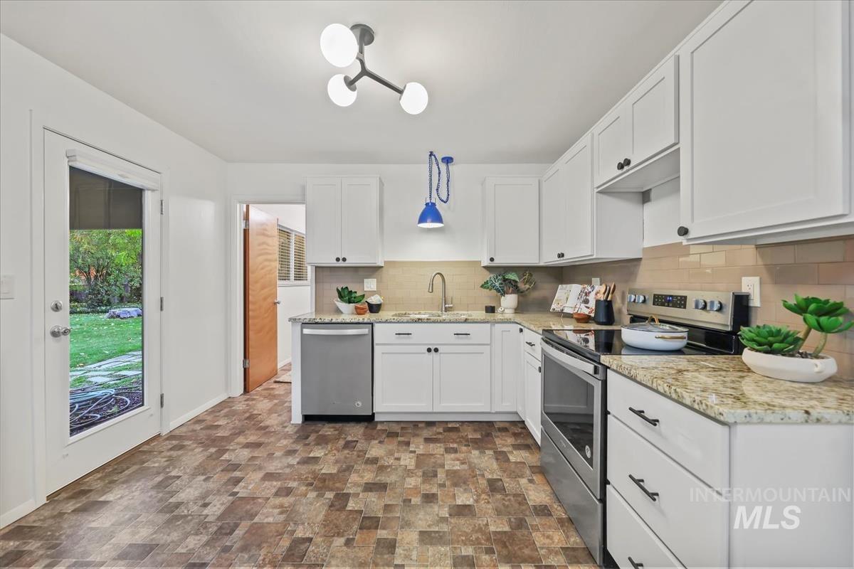 Kitchen featuring appliances with stainless steel finishes, white cabinetry, decorative backsplash, and light stone countertops