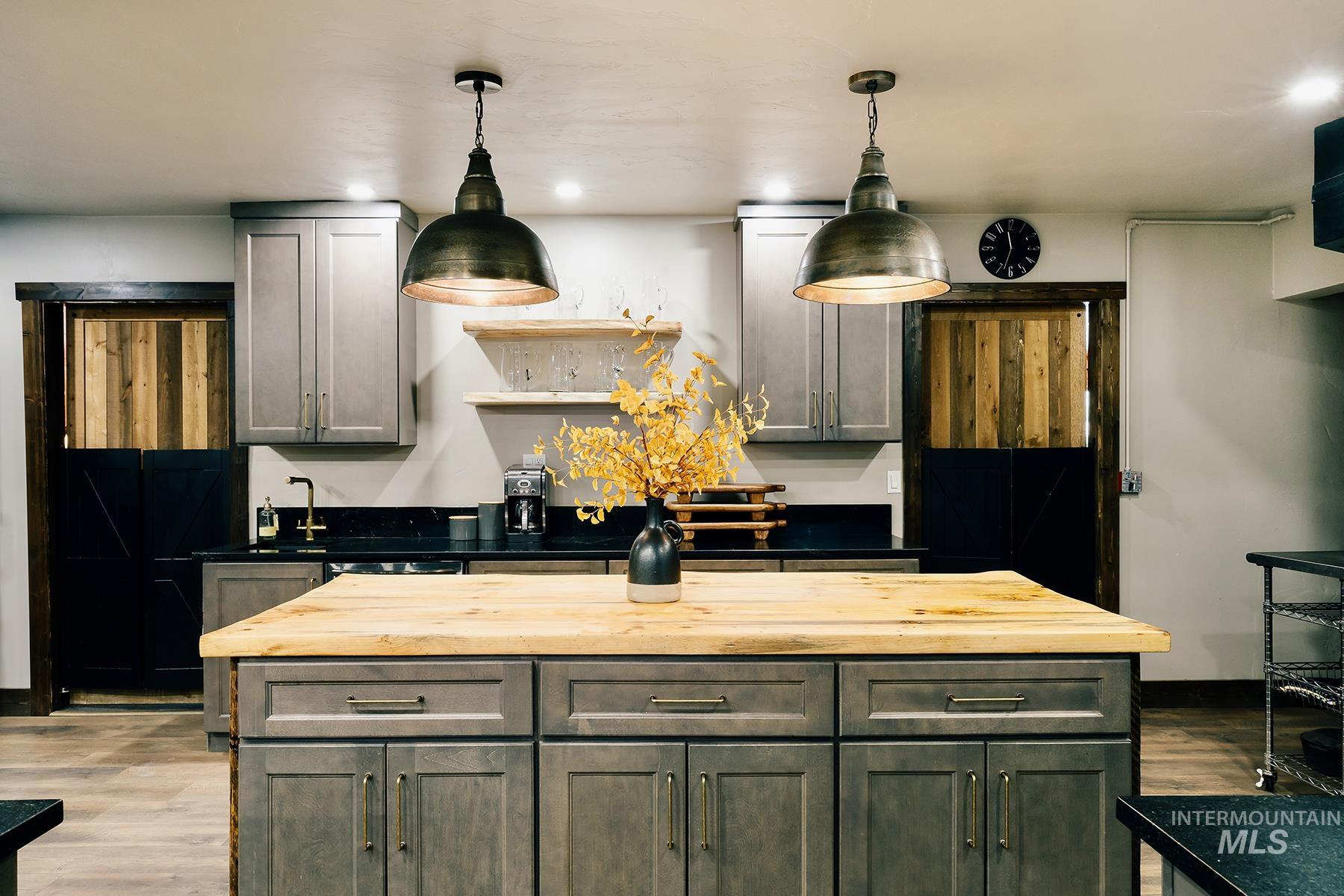 Kitchen featuring decorative light fixtures, wood finished floors, a center island, gray cabinetry, and wood counters