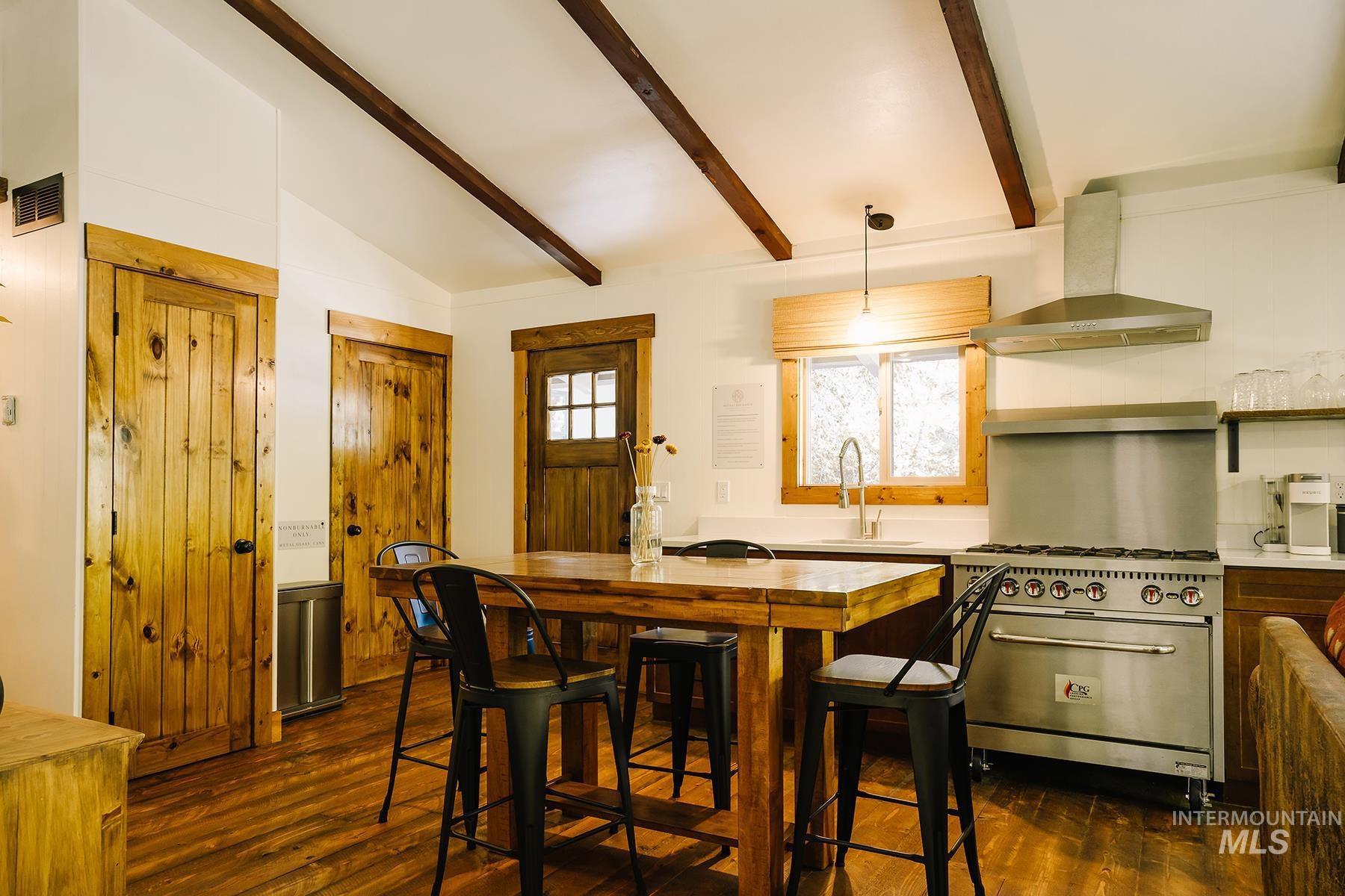 Kitchen featuring dark wood-style floors, wall chimney range hood, stainless steel range with gas stovetop, and hanging light fixtures