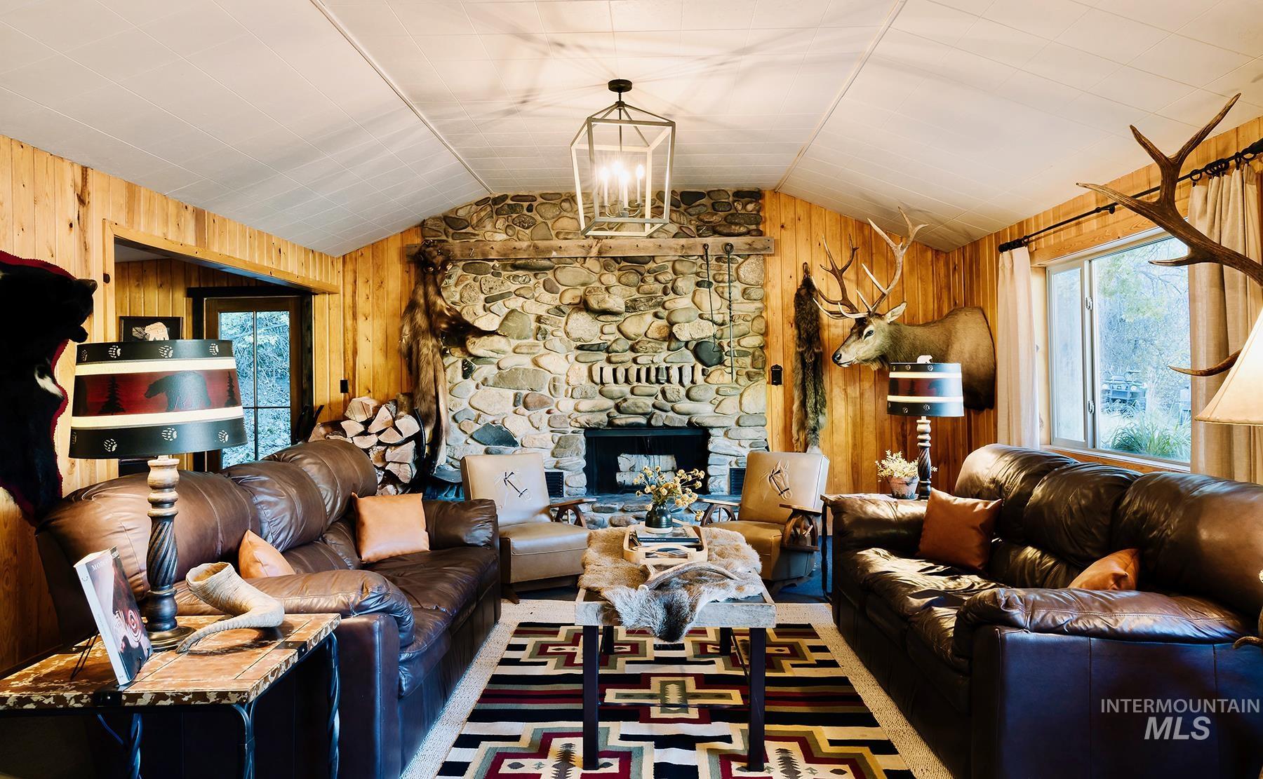 Living room featuring wooden walls, vaulted ceiling, a fireplace, and a chandelier