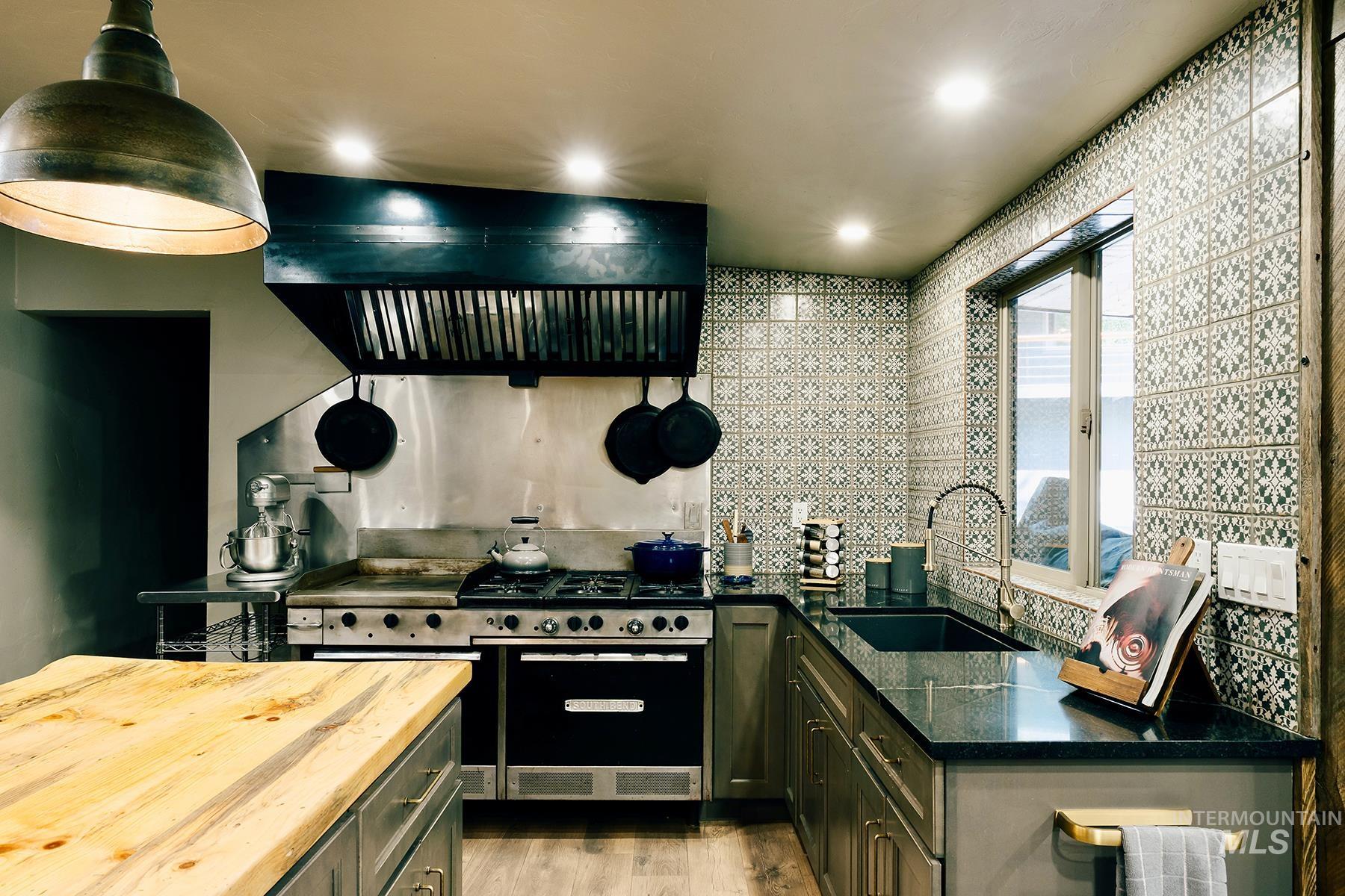 Kitchen with light wood-style flooring, green cabinets, wooden counters, range with two ovens, and ventilation hood