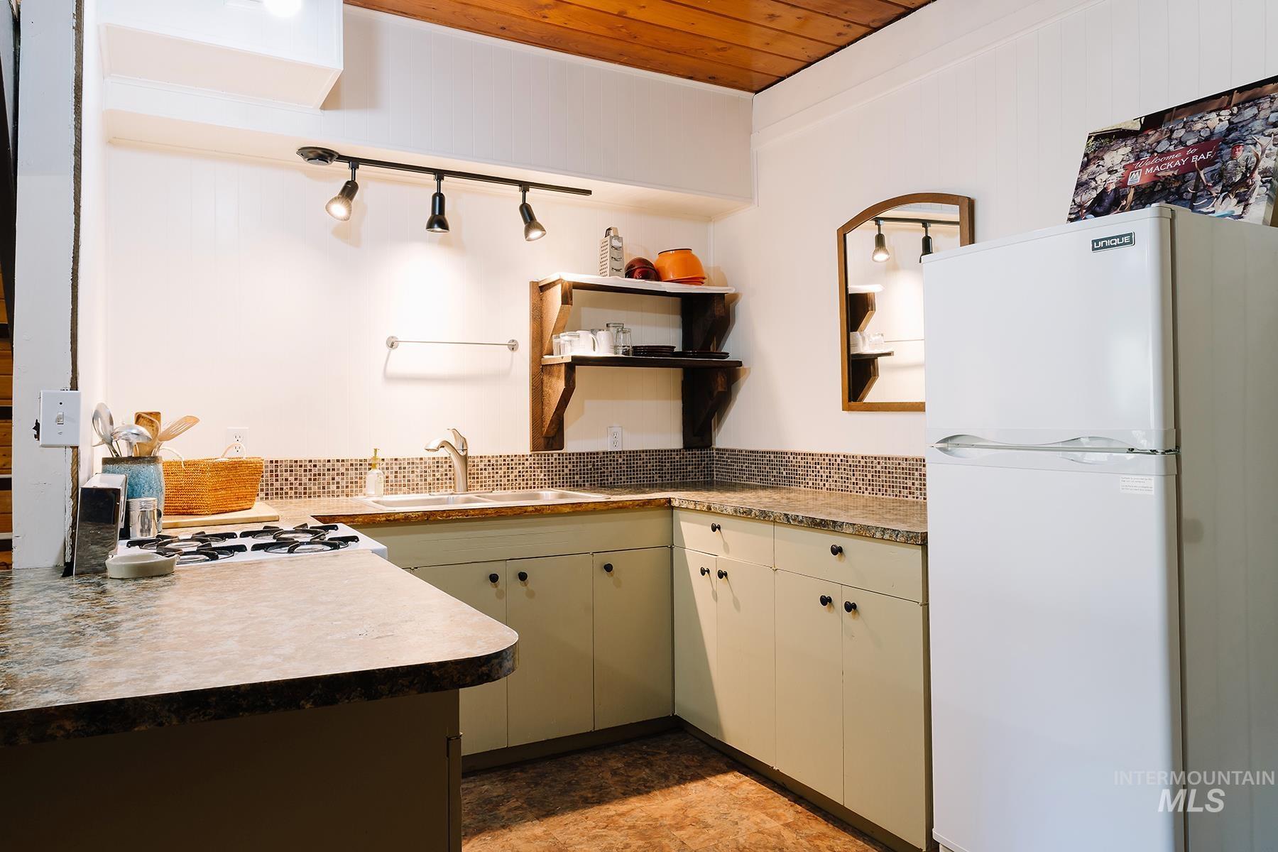 Kitchen with freestanding refrigerator, open shelves, cream cabinets, light countertops, and tasteful backsplash