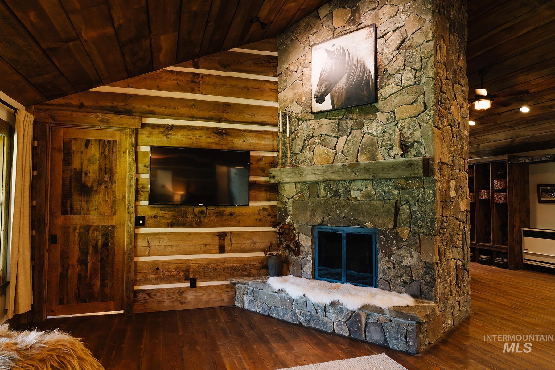 Living room featuring wood ceiling, dark wood-style flooring, a stone fireplace, and lofted ceiling