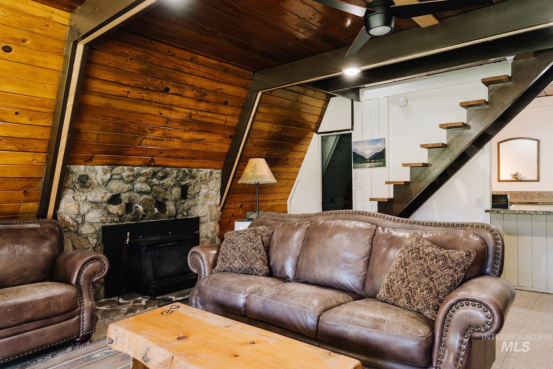 Living room featuring stairway, a ceiling fan, a wood ceiling with exposed beams, and a fireplace