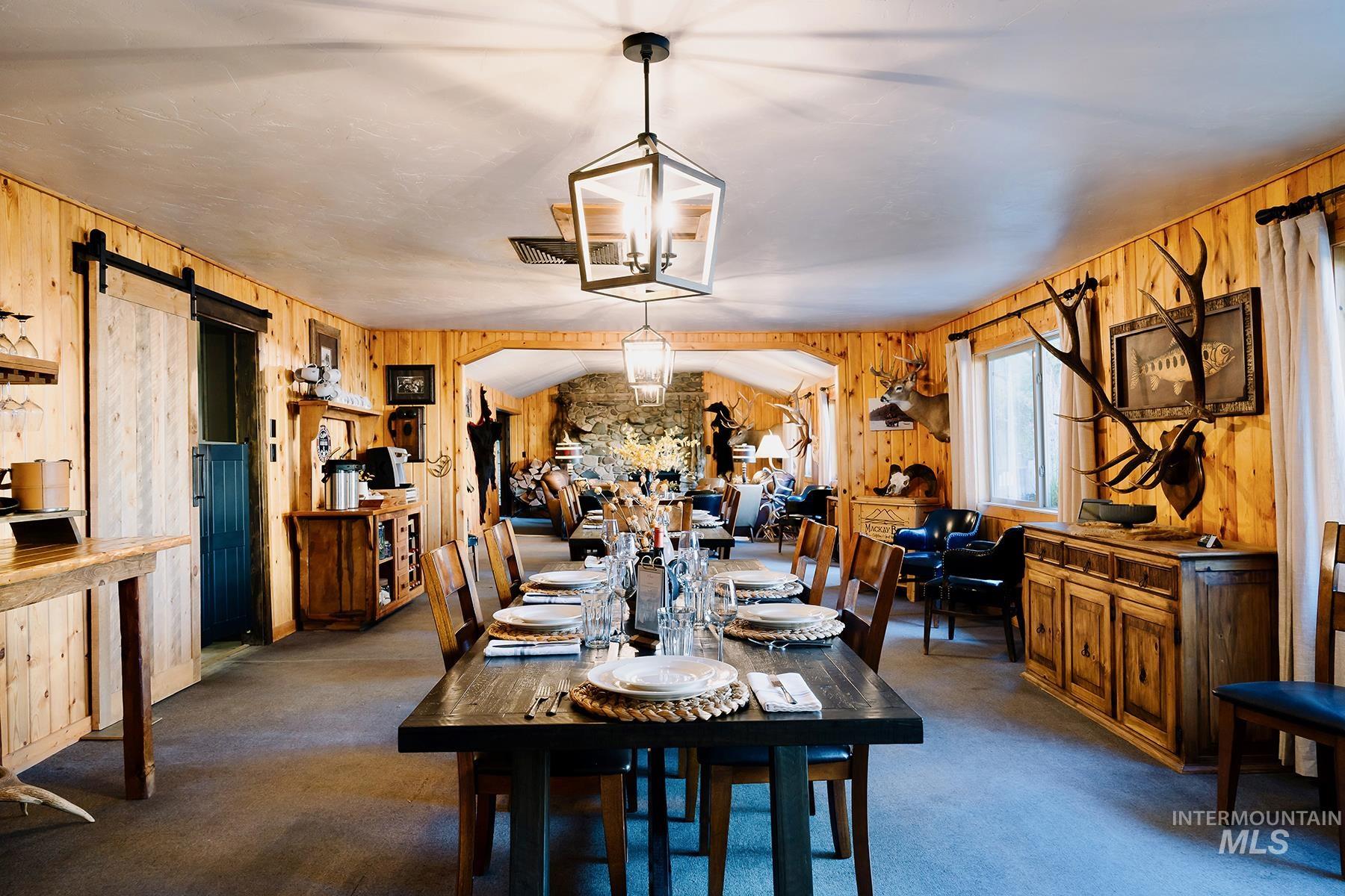 Dining space with wooden walls, a barn door, a chandelier, and dark carpet
