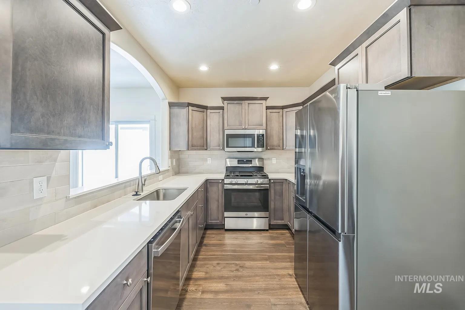 Modern kitchen featuring stainless steel appliances, white countertops, wood-finish flooring, recessed lighting, and an arched pass-through opening
