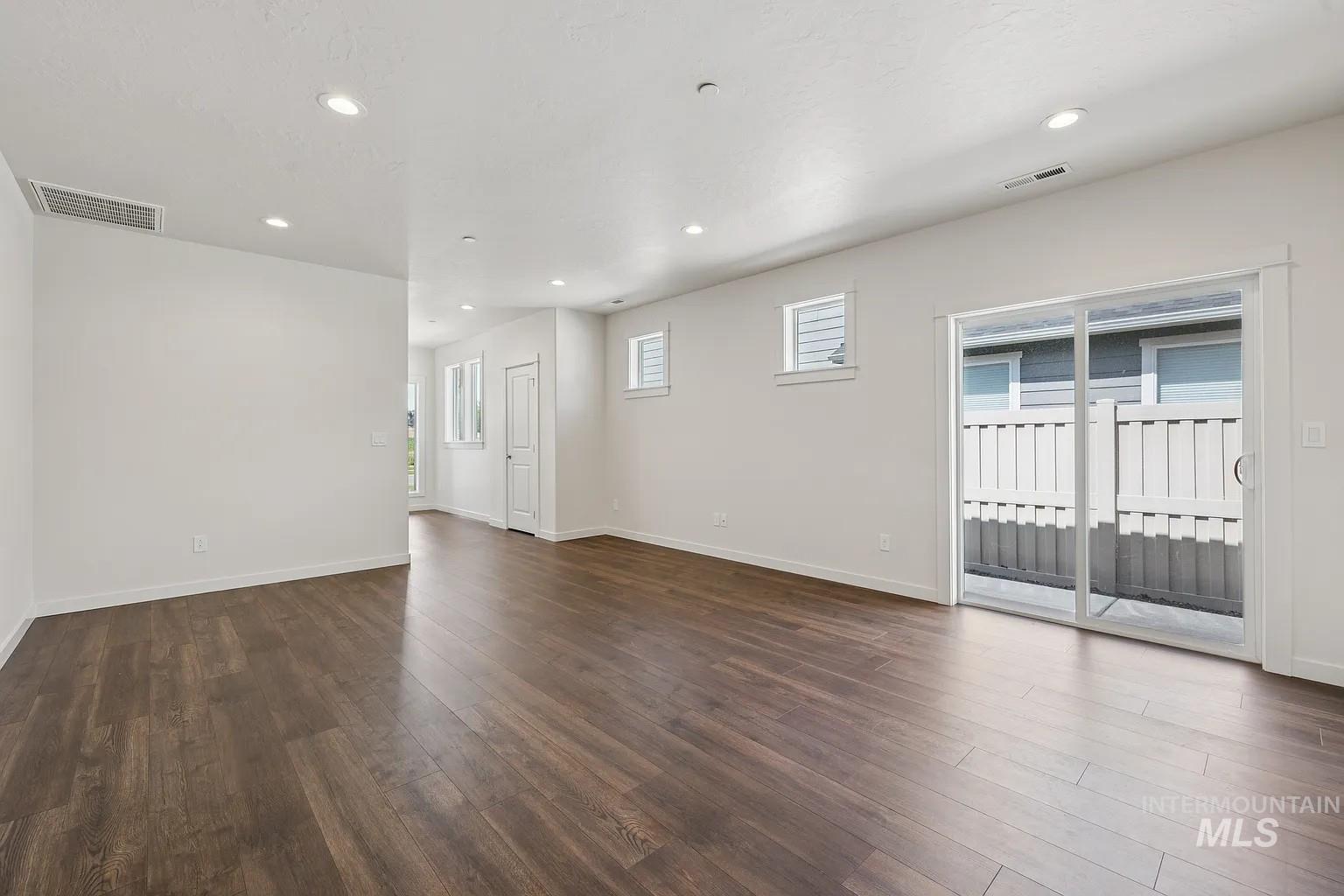 Spacious room featuring wood-finish flooring, white walls, recessed lighting, and a sliding glass door providing exterior access