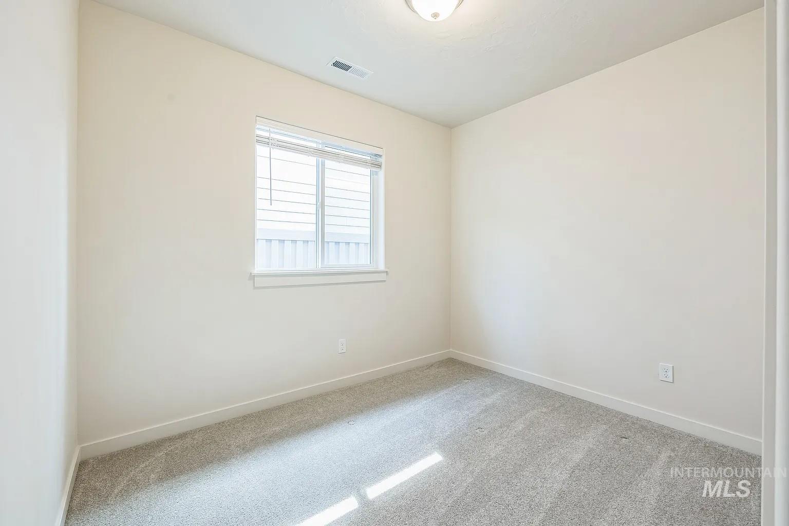 Neutral-toned room featuring a single window with blinds, light gray carpet, and white baseboards